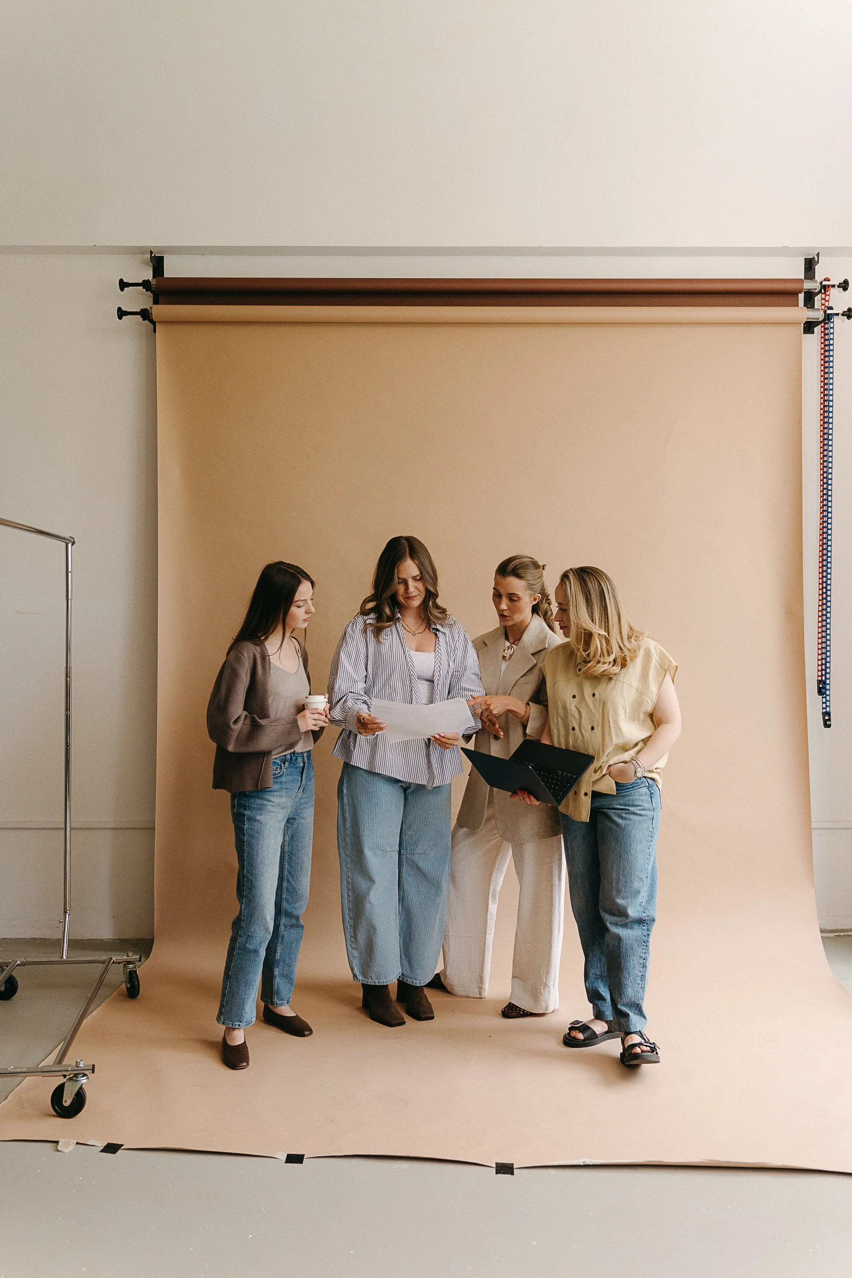 The Finery Media team standing together in front of a beige backdrop, reviewing papers and a laptop.