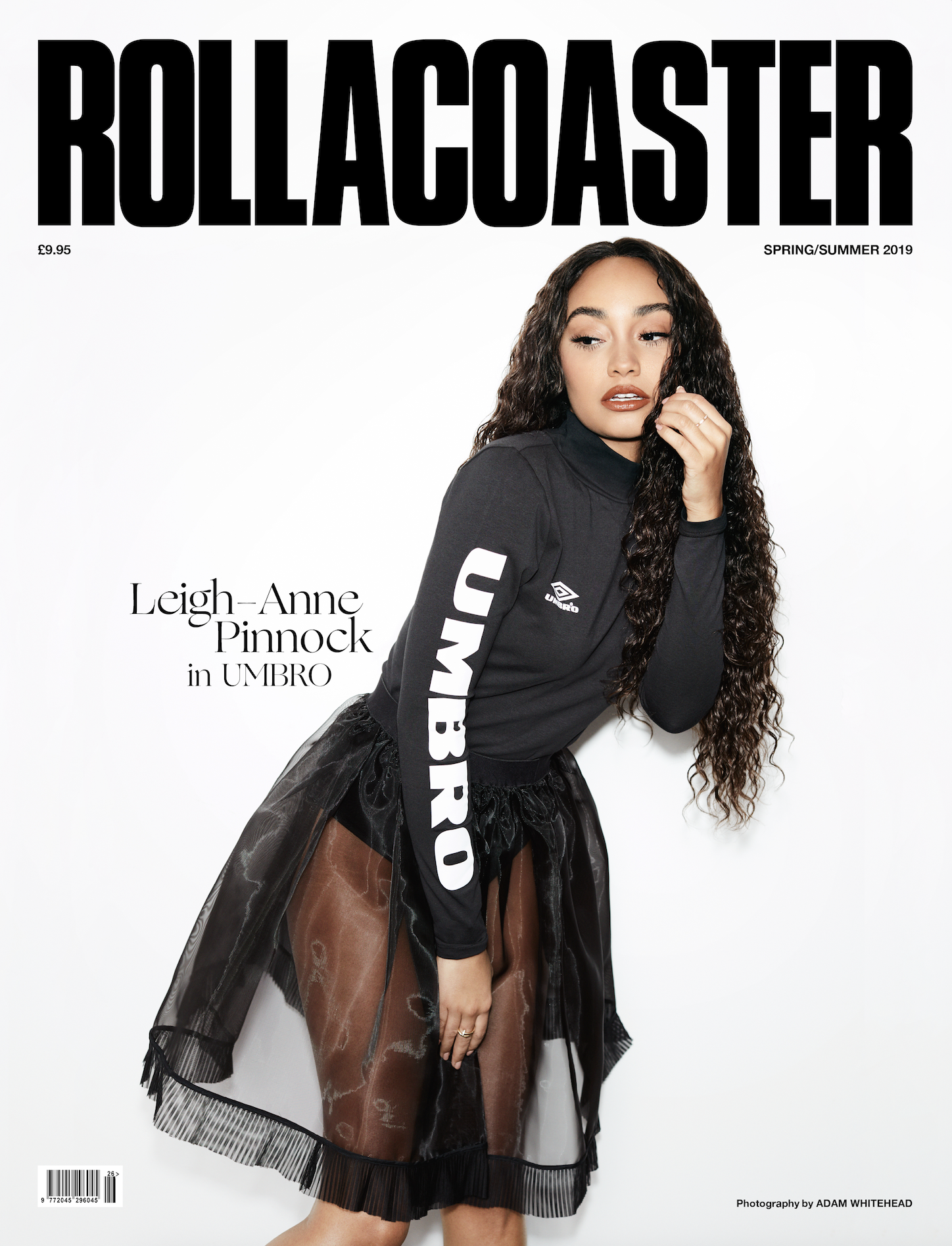 Cover of Rollacoaster magazine featuring a woman with long, curly hair, wearing a black sporty top with white lettering and a sheer skirt, standing against a white background.