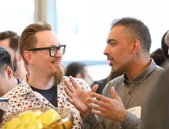 Two men engaged in conversation at a social event, smiling and gesturing.