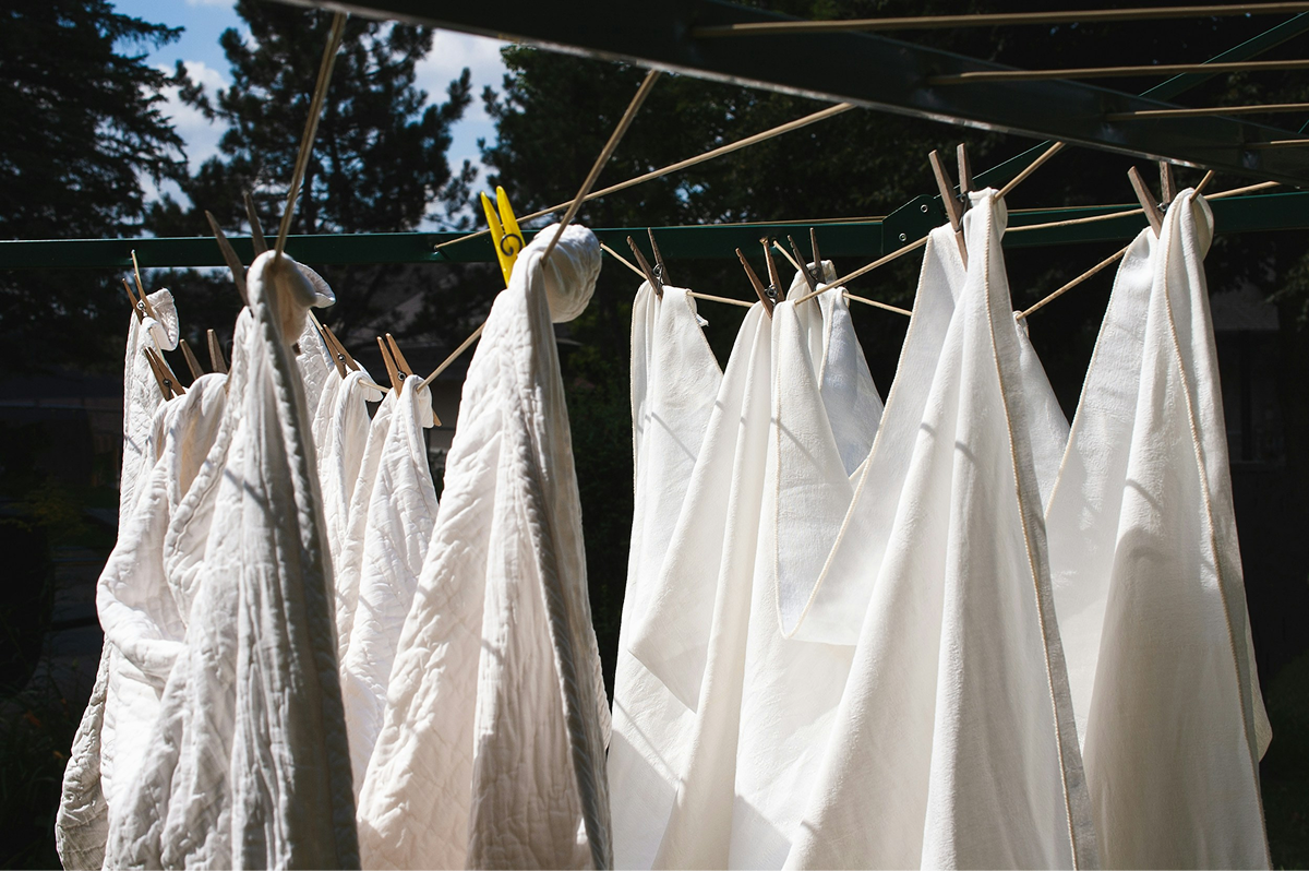 White laundry hanging on a clothesline outdoors with clothespins, sunlight, and trees in the background.
