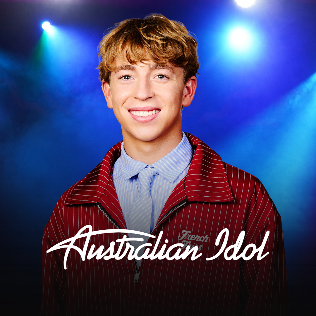Young man smiling in front of colorful stage lights, wearing a red zip-up jacket with white stripes over a blue collared shirt. The text 'Australian Idol' is overlayed on the image.