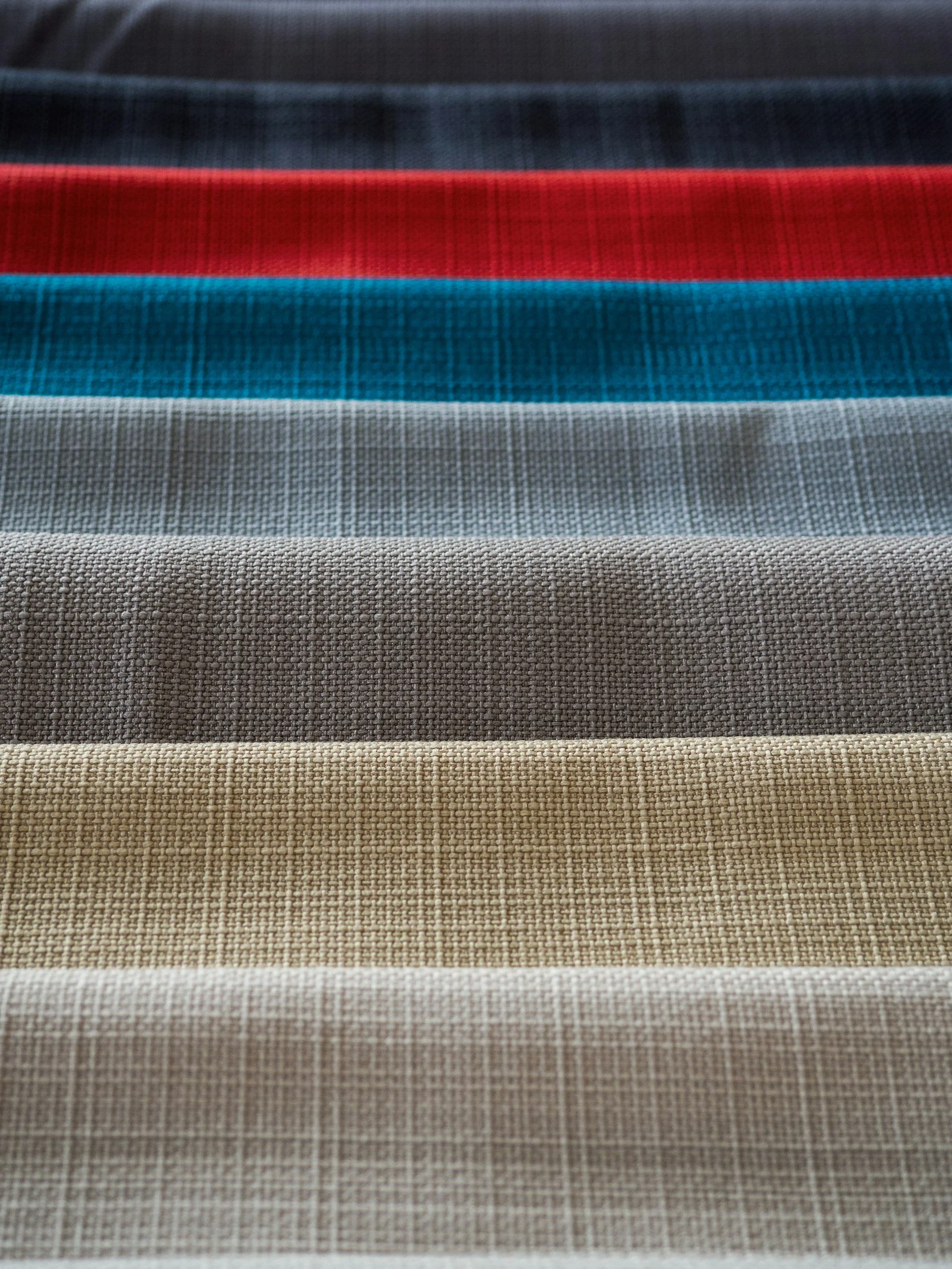 Stack of folded fabric swatches in various colors and textures, including beige, gray, blue, red, dark blue, and teal.