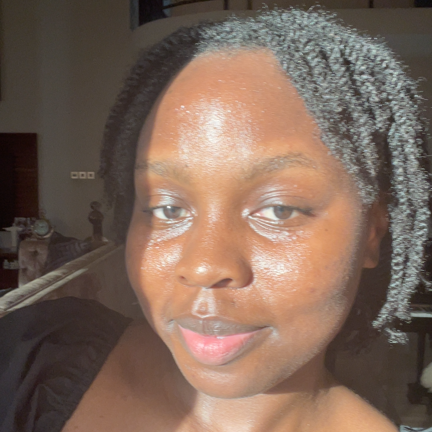 Close-up of a woman with dark skin, short curly gray hair, and light eye makeup, looking into the camera in a dimly lit room.