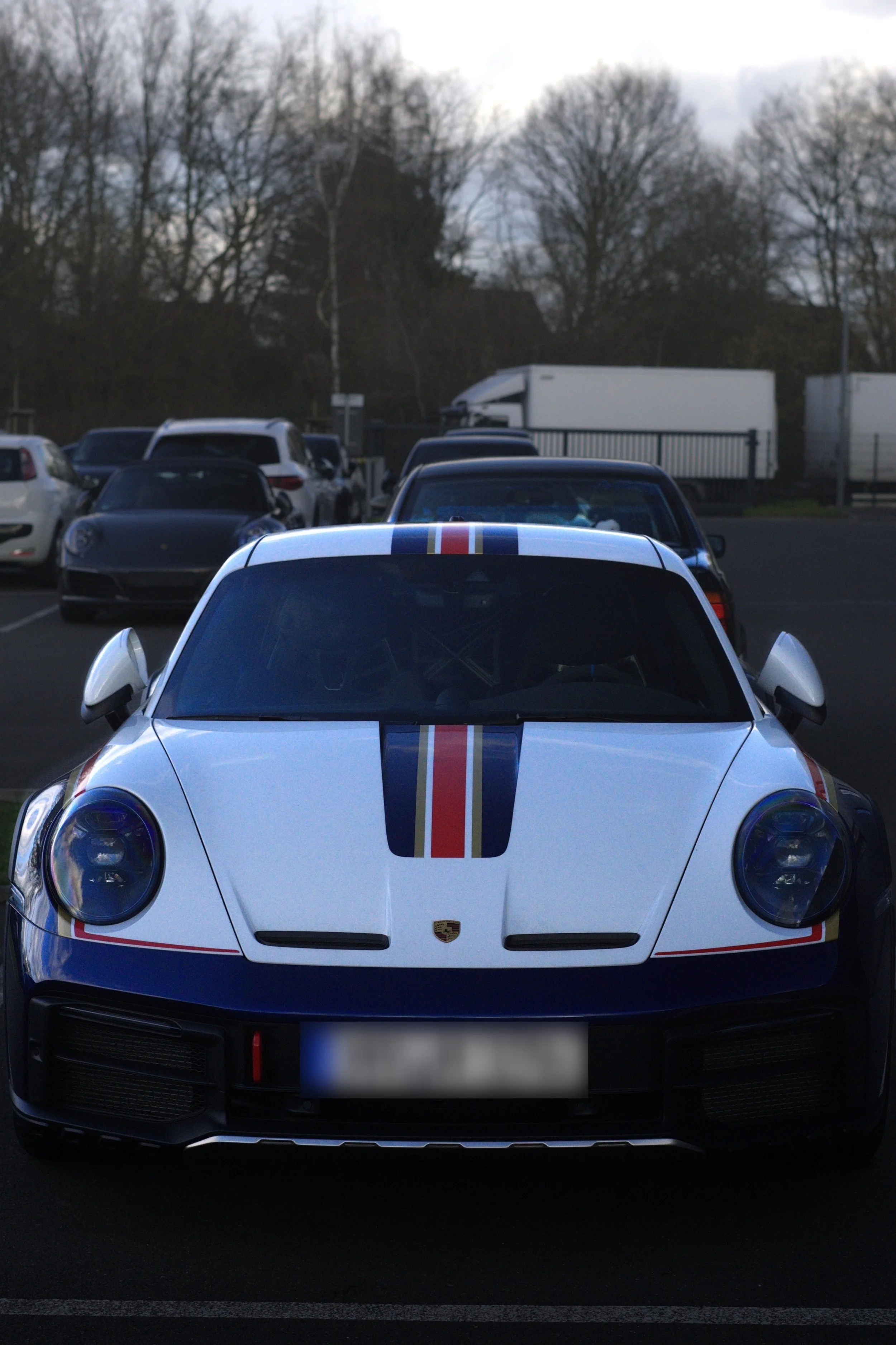Ein weißer Porsche 911 mit einem roten, blauen und goldenen Streifen in einem Parkplatz.