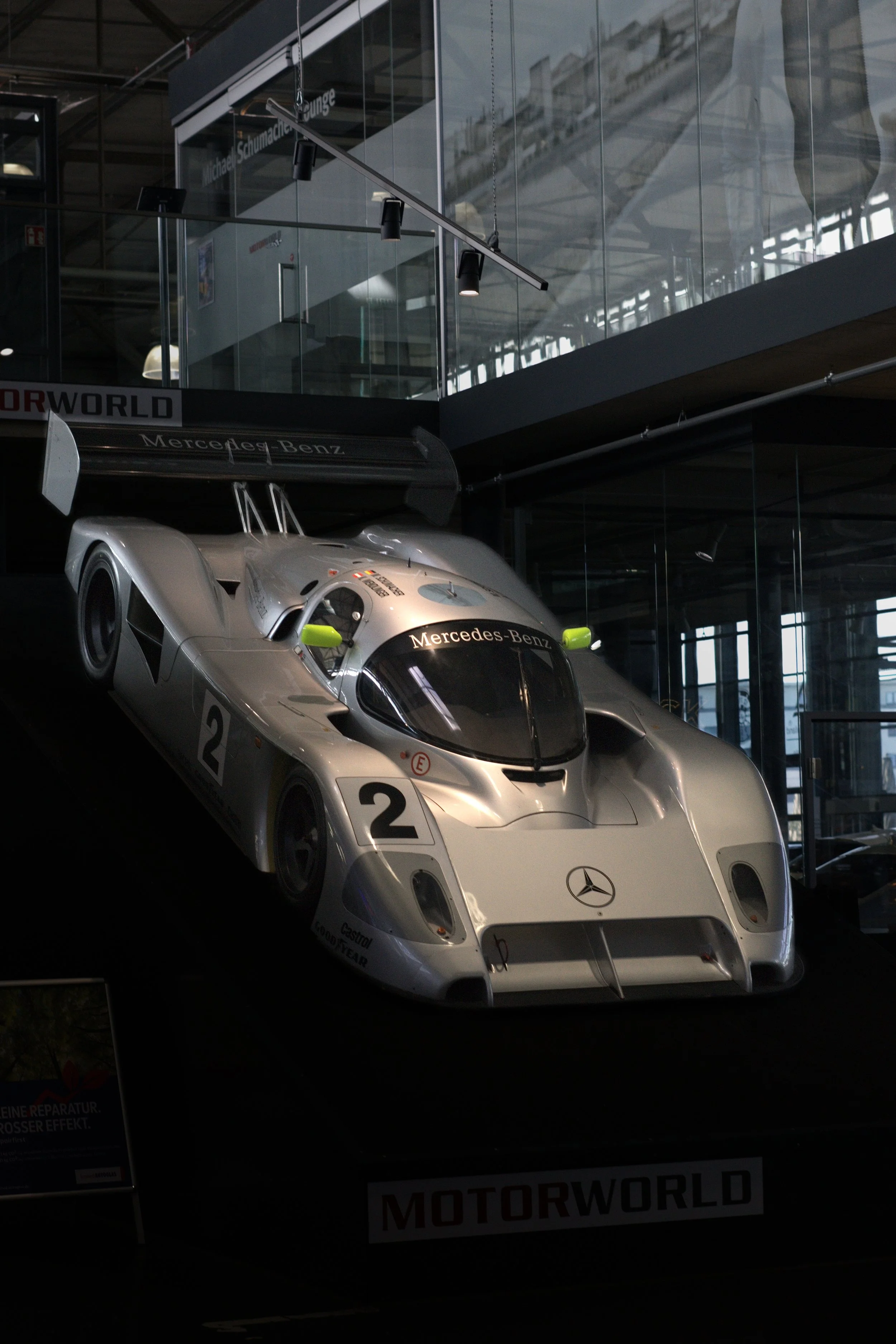 Ein silberner Rennwagen mit Mercedes-Benz Logo auf einem Ausstellungsdisplay in einem Museum, das Fahrzeug ist für den Motorsport bestimmt.