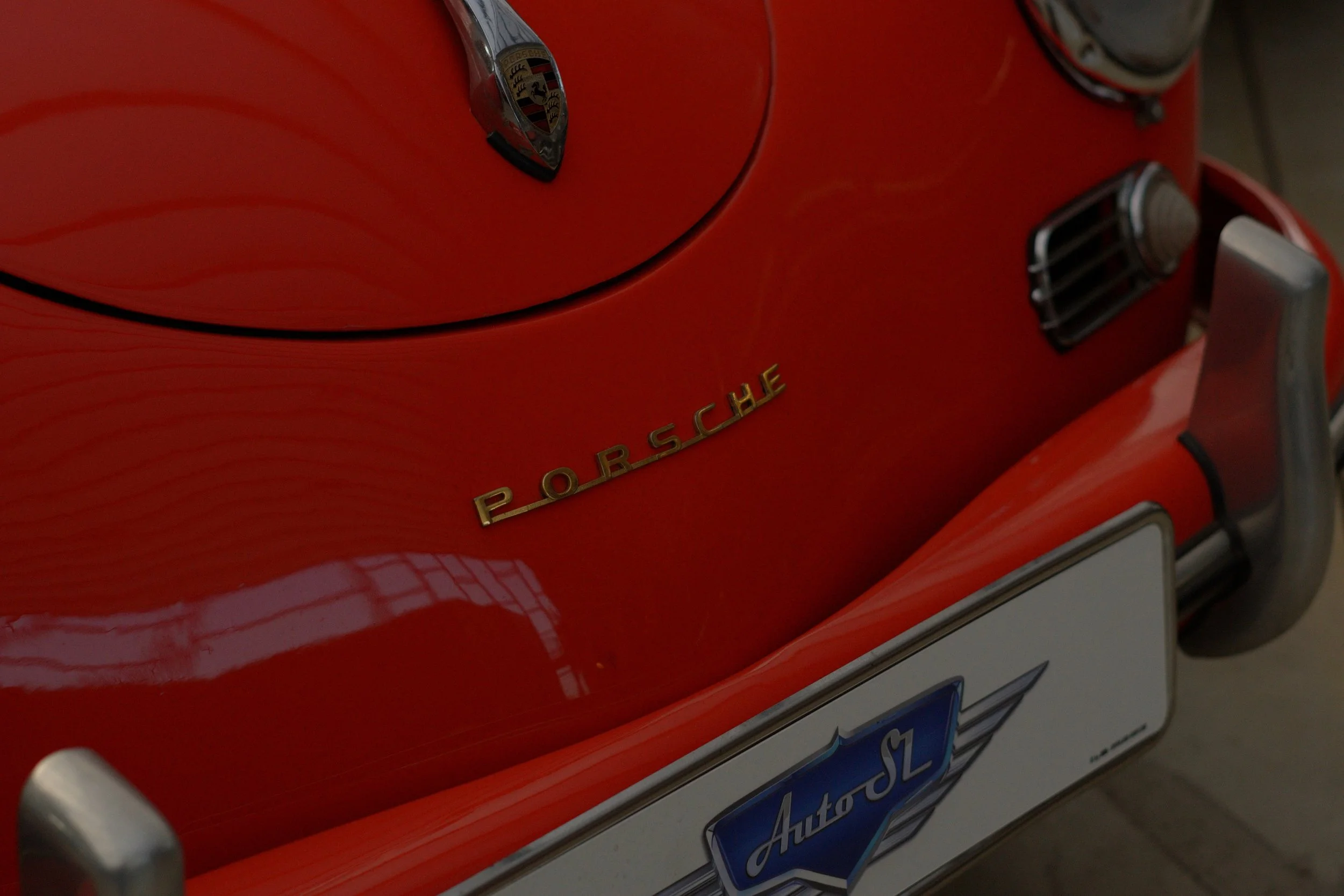 Nahaufnahme des vorderen Teils eines roten Porsche-Sportwagens, inklusive Porsche-Emblem, Scheinwerfer, Kühlergitter und Nummernschild.