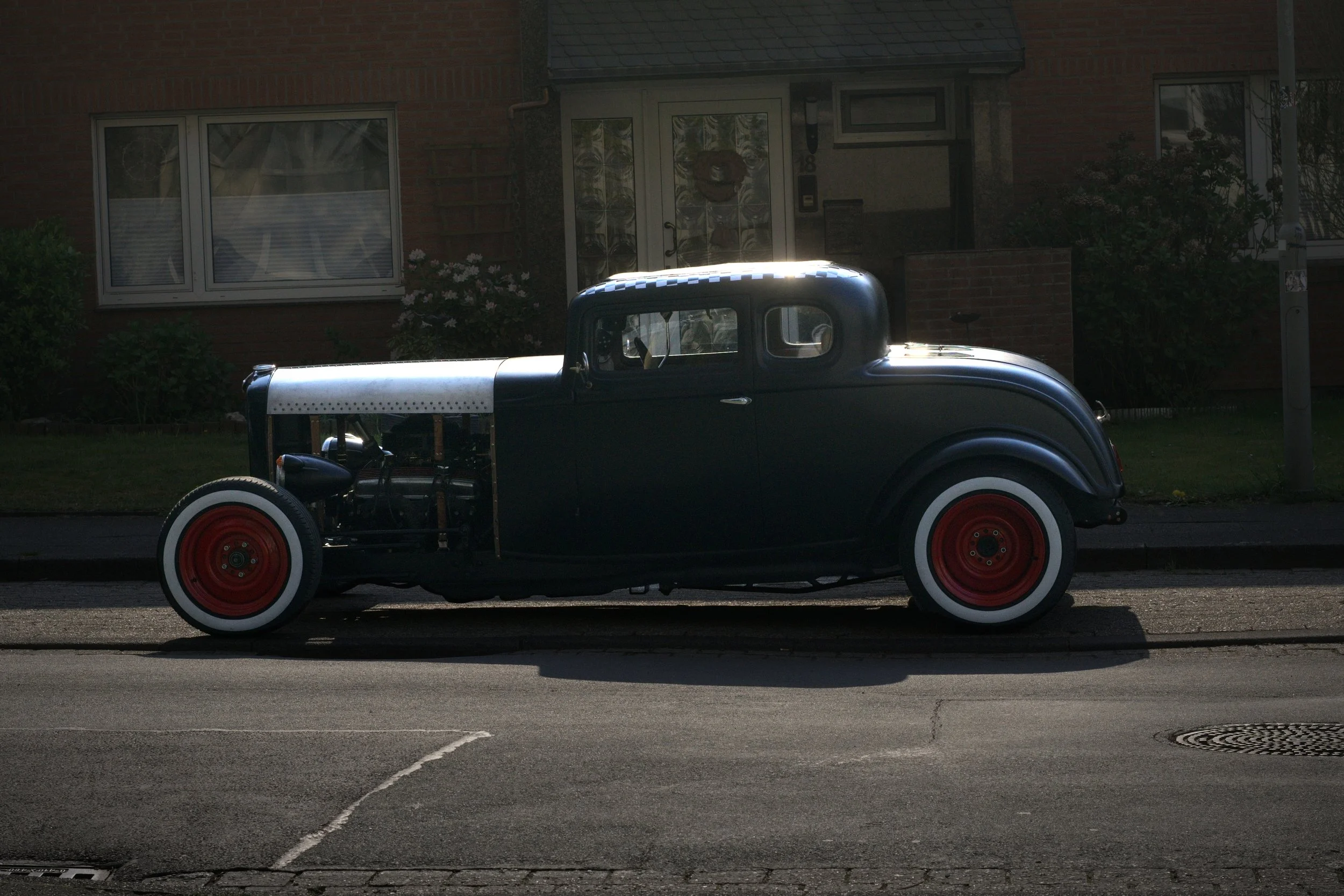 Ein alter, schwarzer Automobil mit roten Rädern, das an einem Gehweg in einer Wohnstraße parkt.
