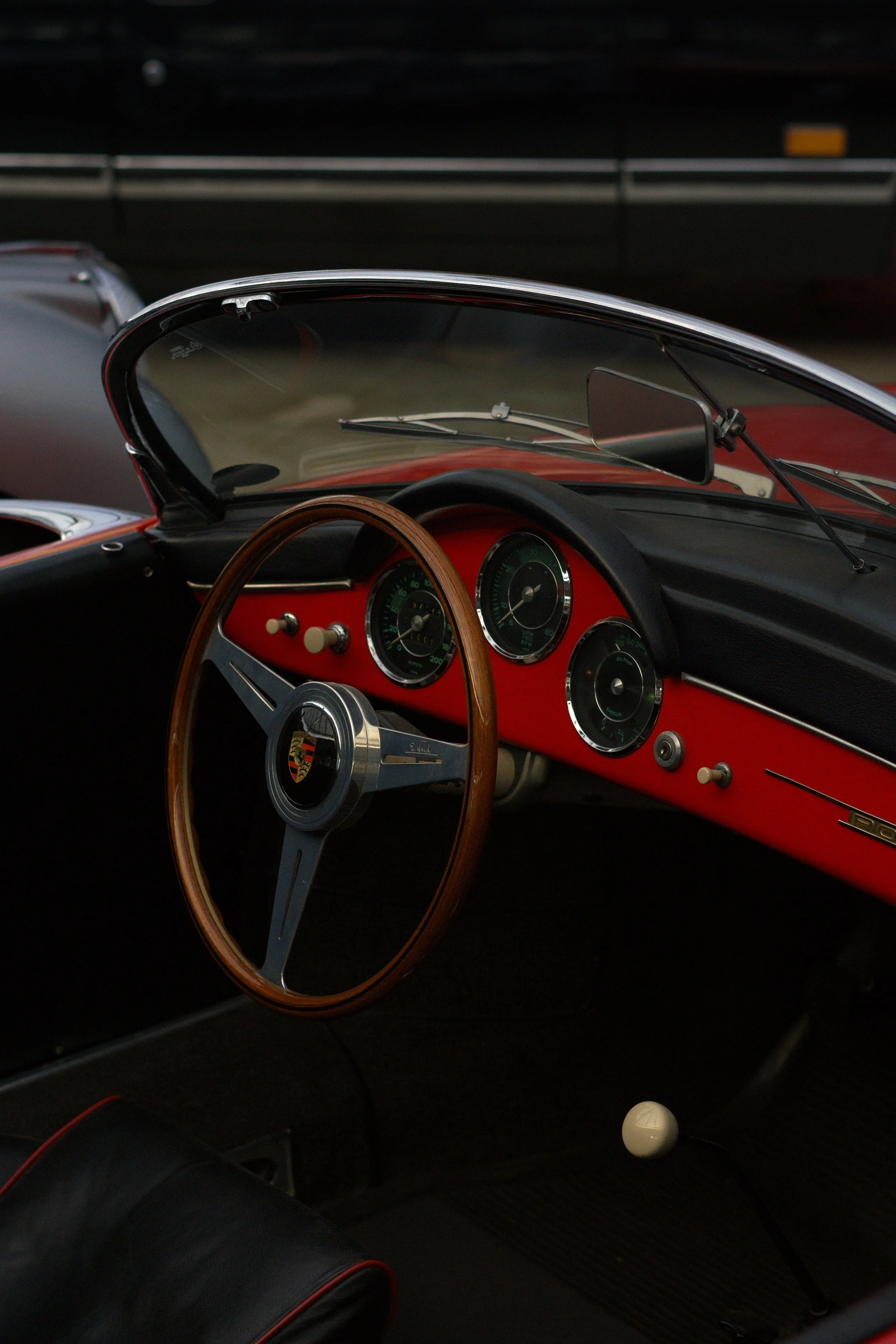 Innenansicht eines klassischen Porsche-Cabriolets mit Holzlenkrad, roten Armaturenbrett und schwarzen Sitzpolstern.