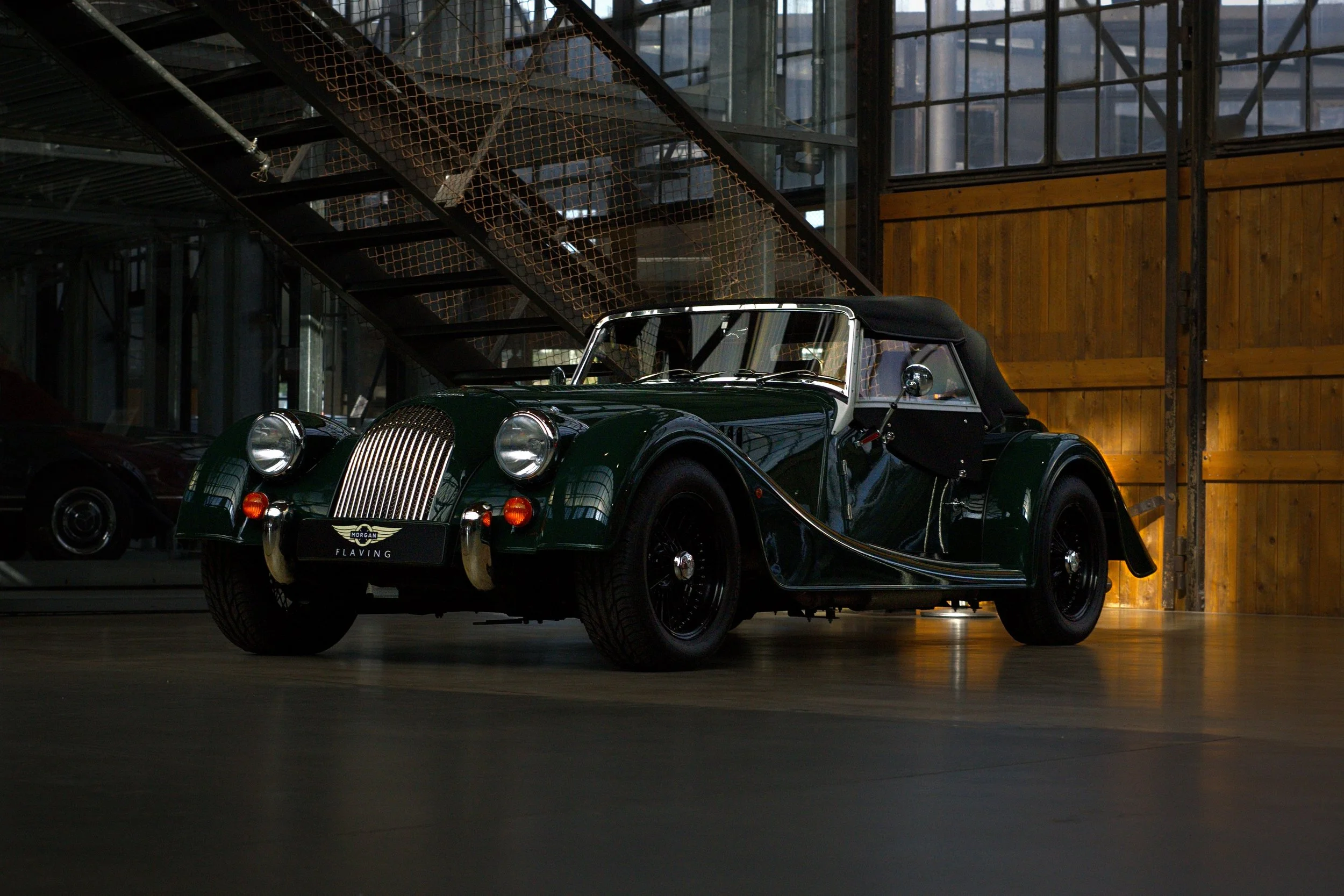 Ein klassischer grüner Morgan Roadster mit schwarzem Verdeck im Museum, im Hintergrund eine Holz- und Metall-Galerie.