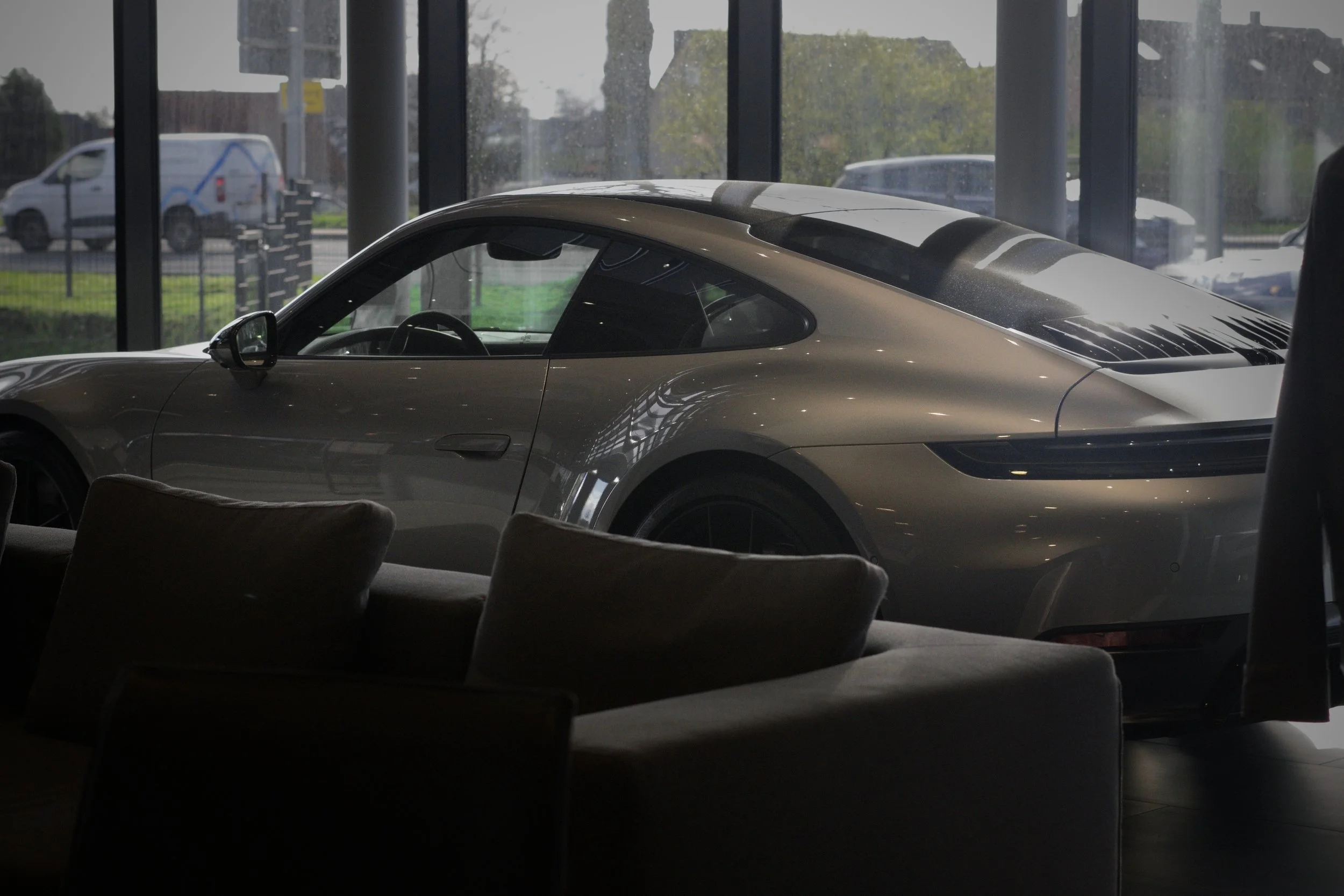 Ein silberner Sportwagen, vermutlich ein Porsche, steht in einem Autohaus vor großen Fenstern.