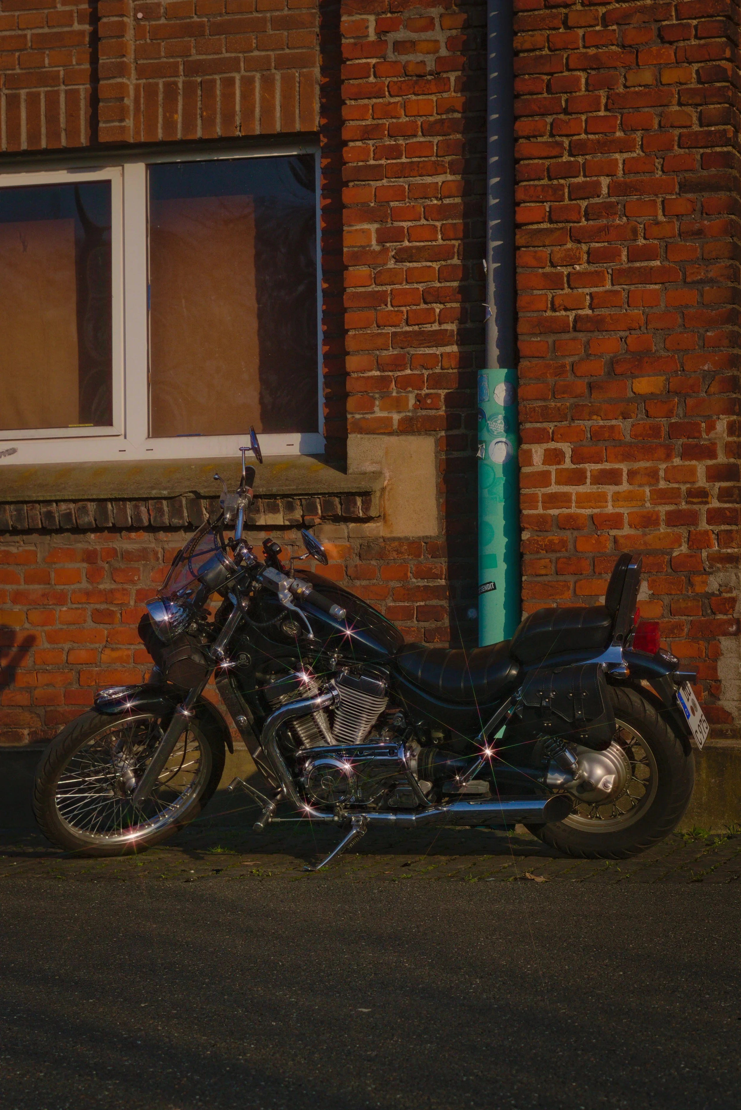 Schwarze Motorradparker an einer roten Backsteinwand mit Fenster und blauer Regenrinne.