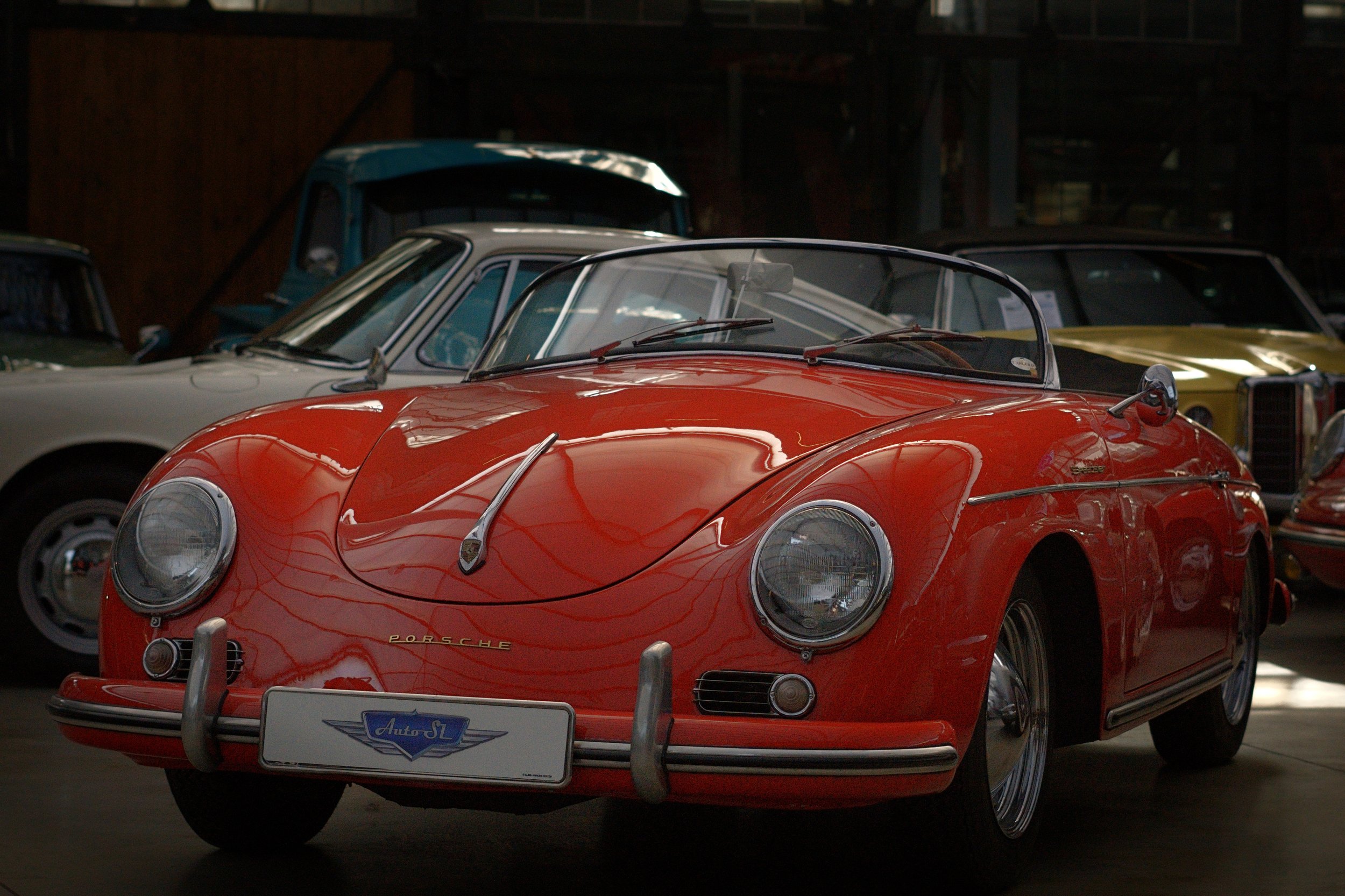 Roter Porsche-Sportwagen mit abnehmbaren Dach in einem Museum, umgeben von anderen klassischen Autos.