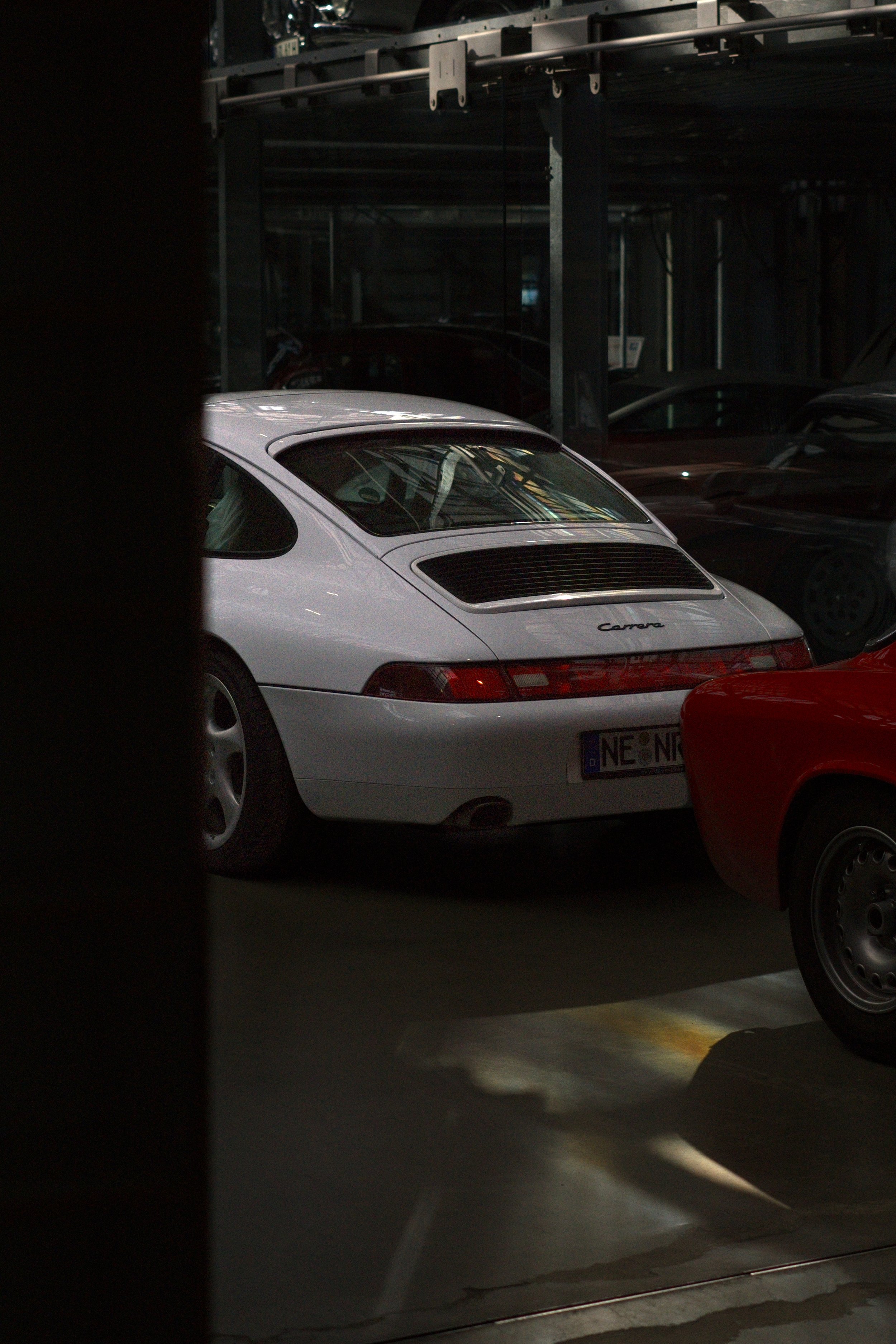 Ein weißer Porsche 911 Carrera im dunklen Parkhaus, umgeben von anderen Autos.