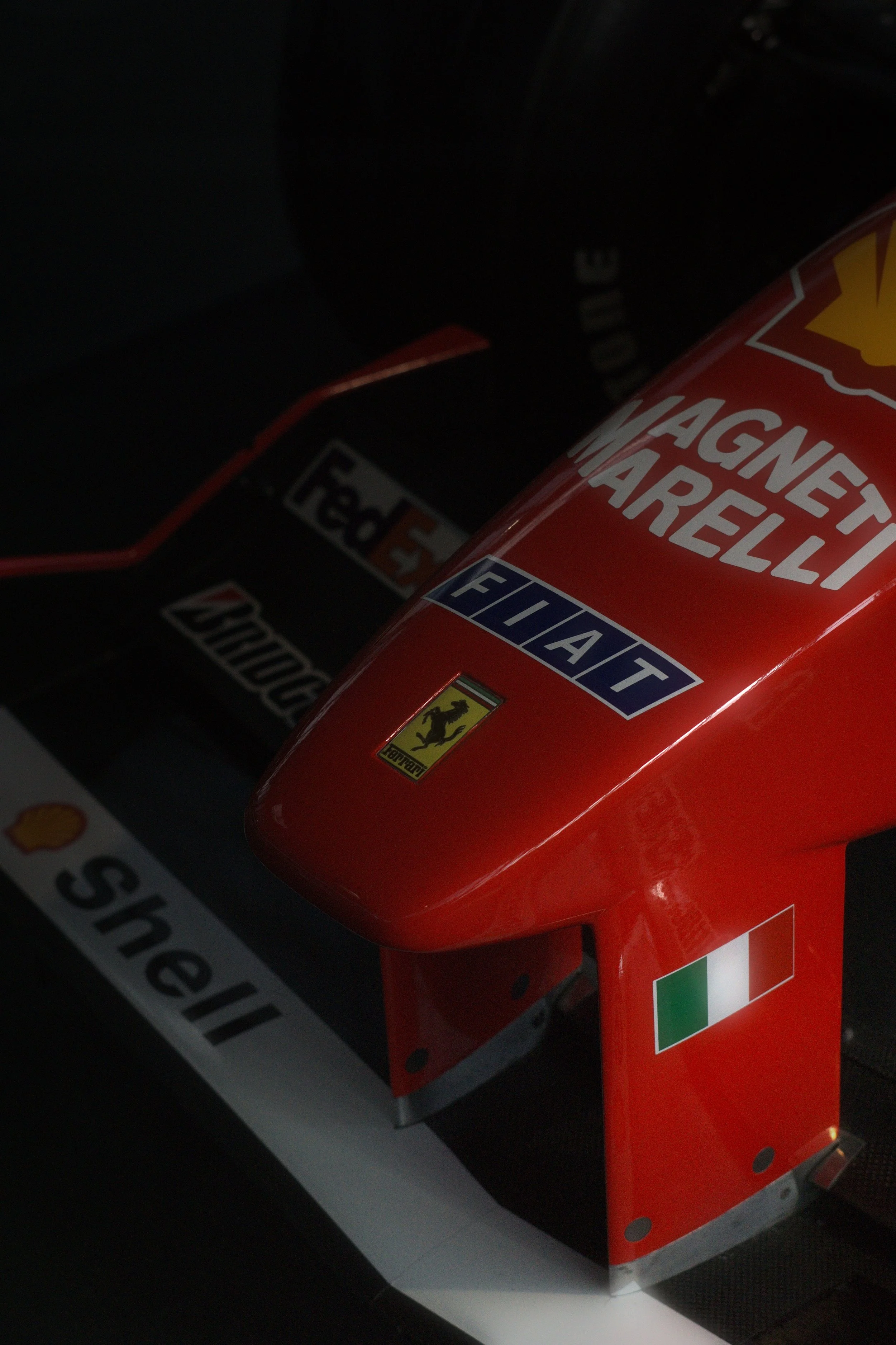 Detail eines roten Ferrari-Formel-1-Autos mit Sponsoren-Logos, darunter Shell, Ferrari, Magneti Marelli, Fiat, Bridgestone und ein italienischer Flaggenaufkleber.