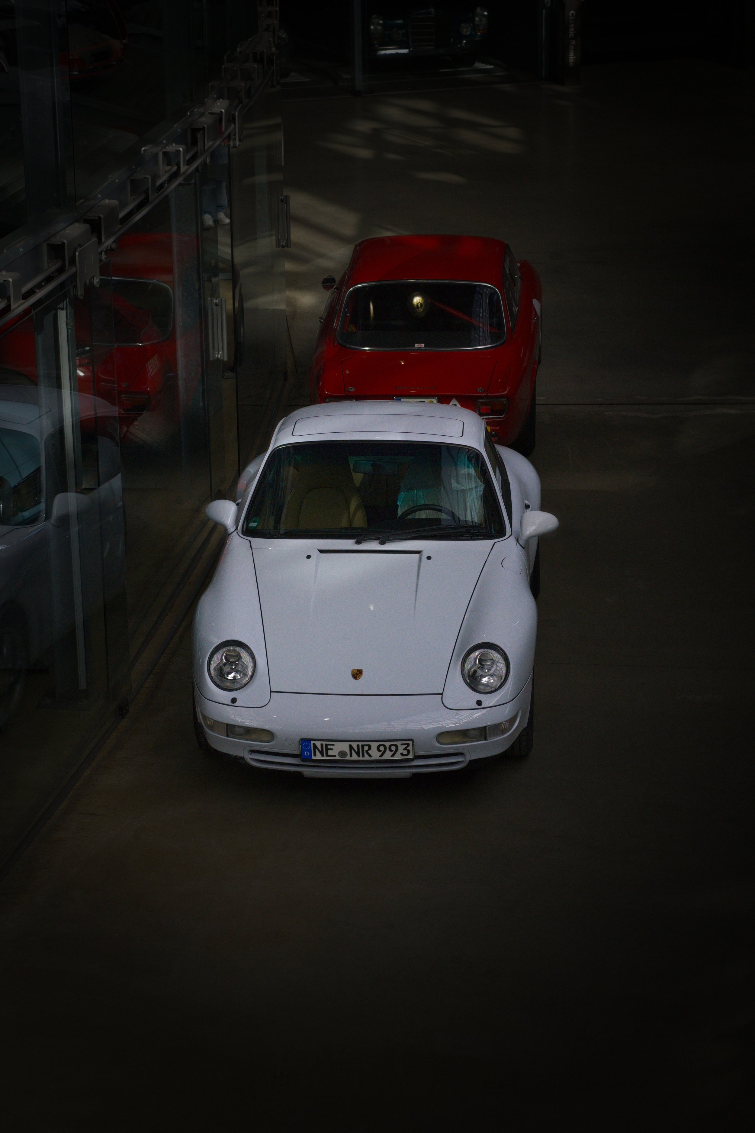 Ein weißer Porsche 911 vor einem roten Porsche 911 in einer Autohalle.