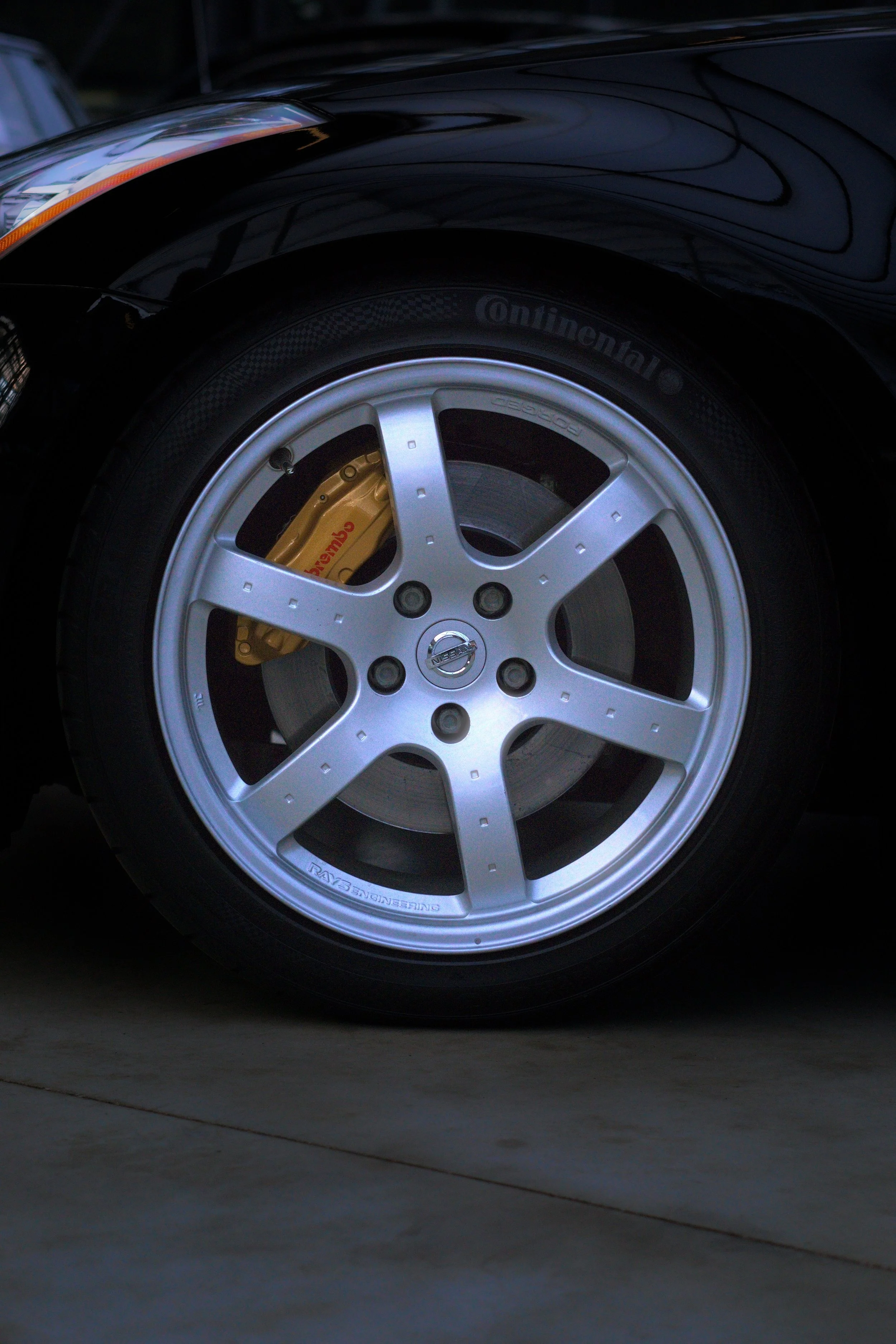 Nahaufnahme eines schwarzen Autos mit silberner Felge, grün-gelber Bremssattel, Continental-Reifen und Nissan-Logo in der Mitte der Felge.