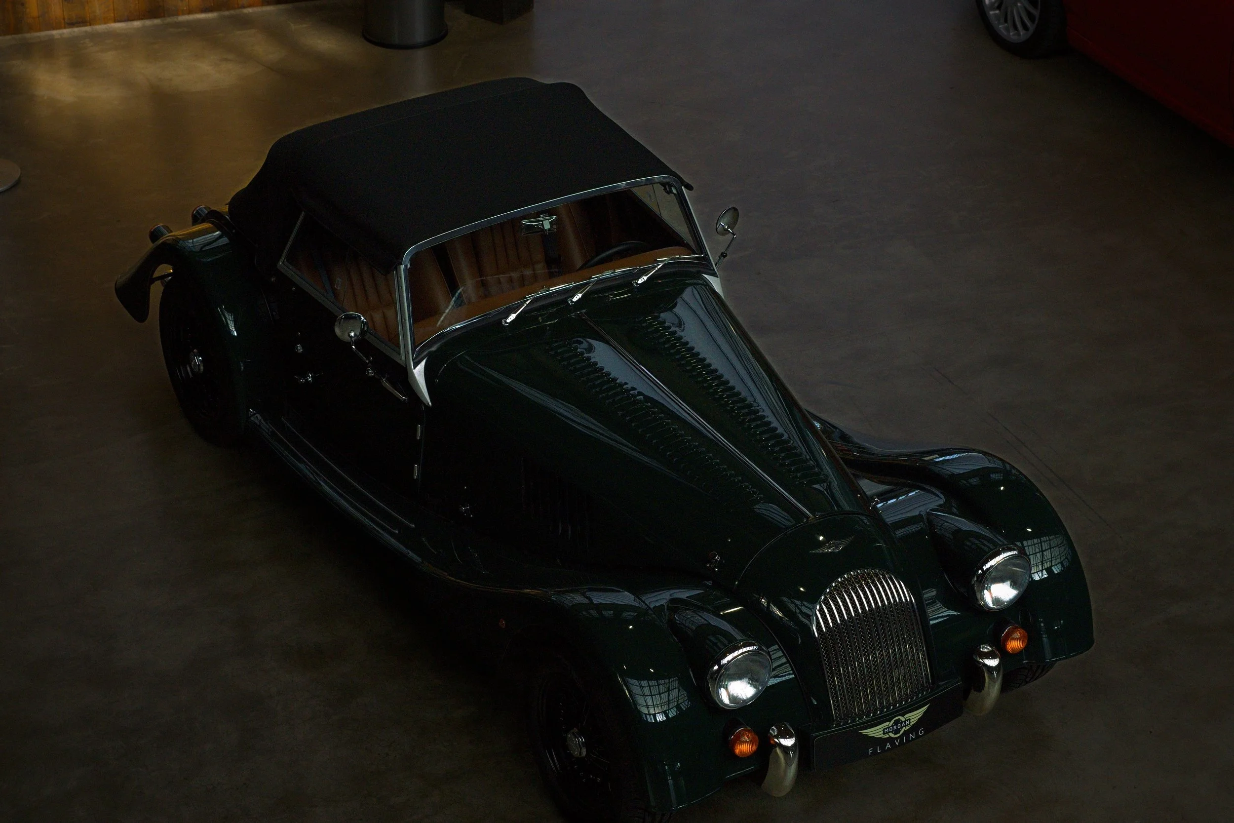Ein schwarz-grüner Oldtimer mit Verdeck, auf einem dunklen Boden in einer Halle geparkt.