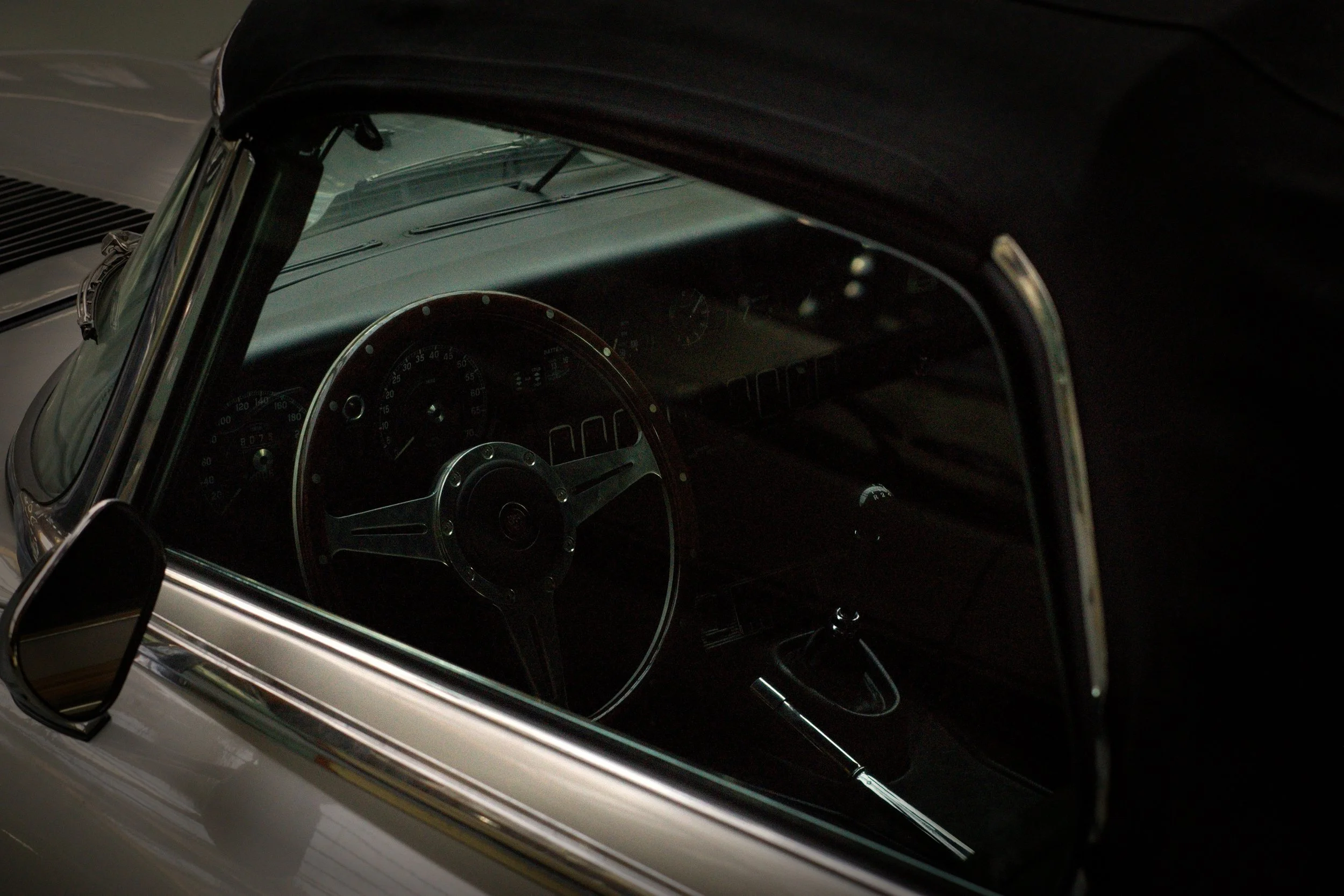 Innenansicht eines klassischen Autos mit Blick auf das Lenkrad und das Armaturenbrett, erhältlich in dunklen Schattierungen.