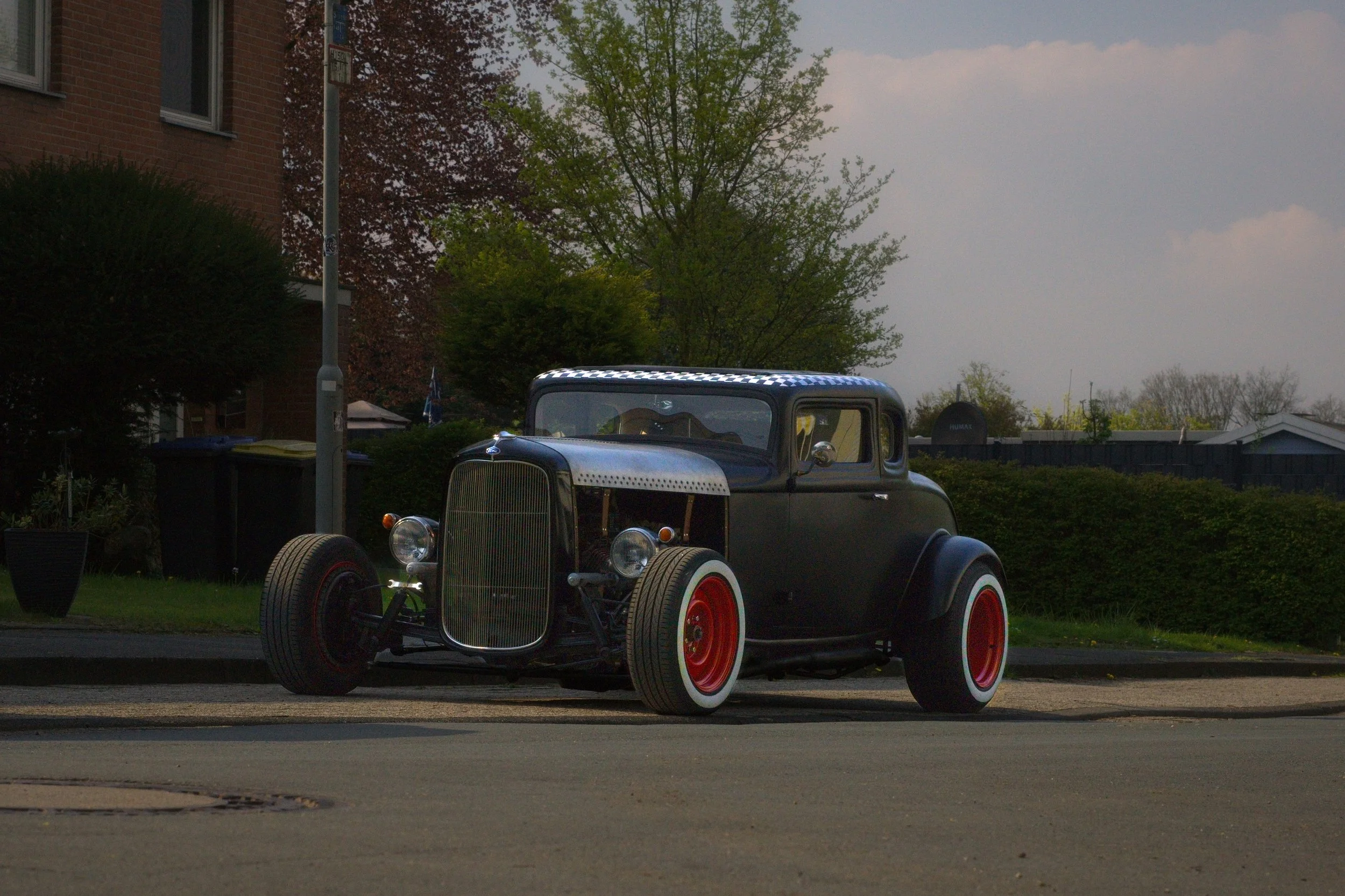 Ein schwarz lackierter, alter Hot Rod mit roten Rädern, parkend am Straßenrand.