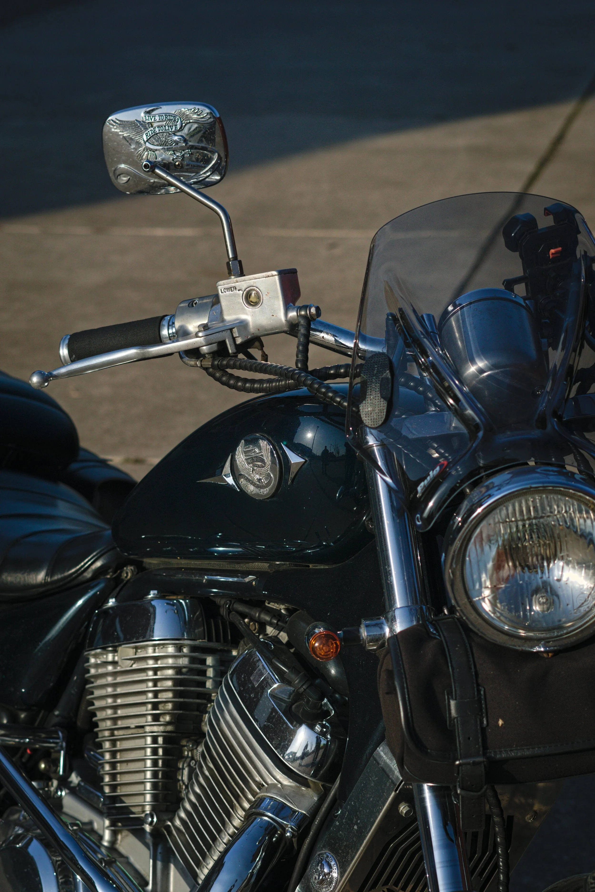 Nahaufnahme eines schwarzen Motorrads mit Chromteilen, einem Scheinwerfer und einem Windschutz. Spiegel zeigt ein eagle-Design mit der Aufschrift "Live to Ride, Ride to Live."