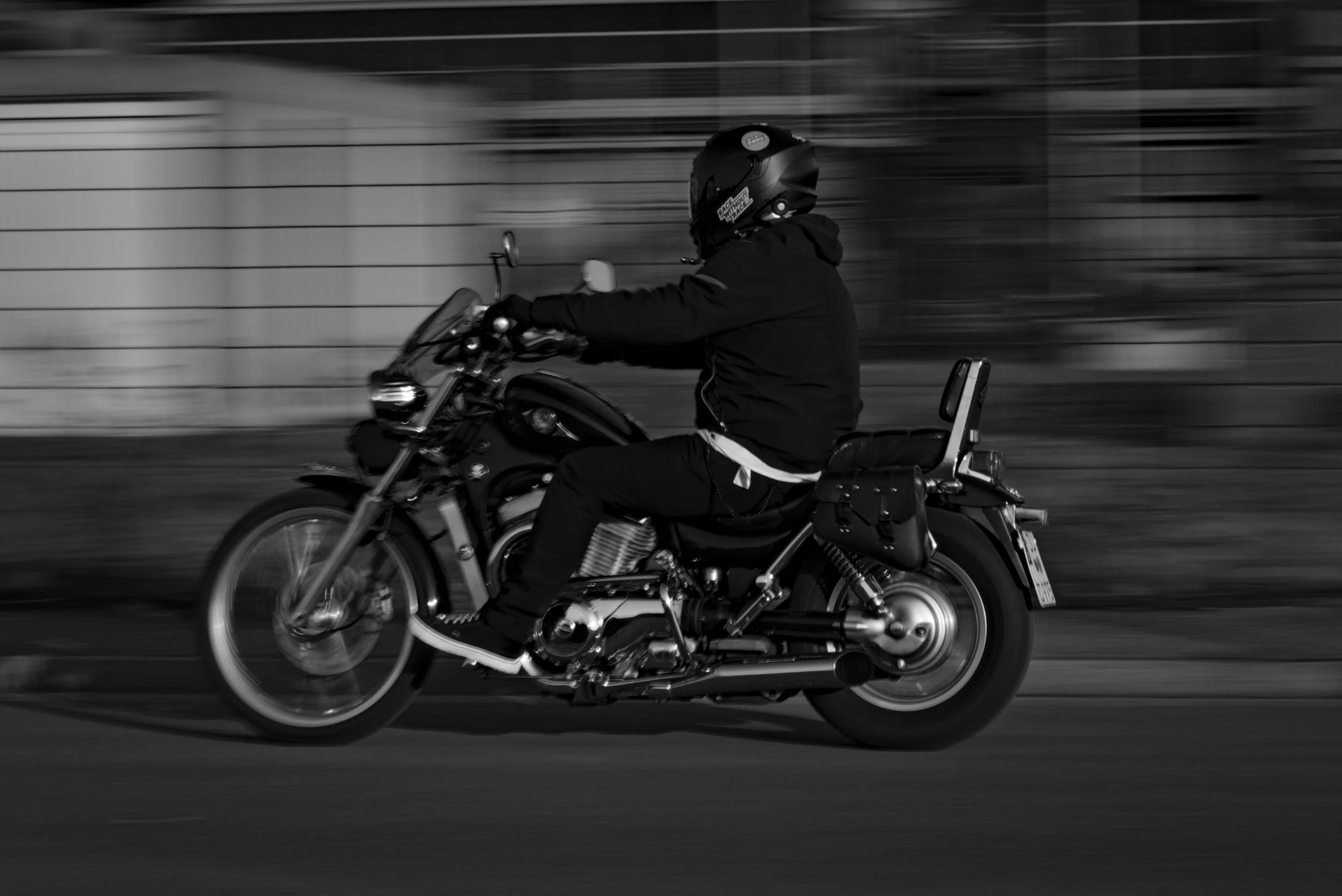 Motorradfahrer in Schwarzhelm fährt auf einer Straße, Bild in Schwarz-Weiß, Bewegungseffekt