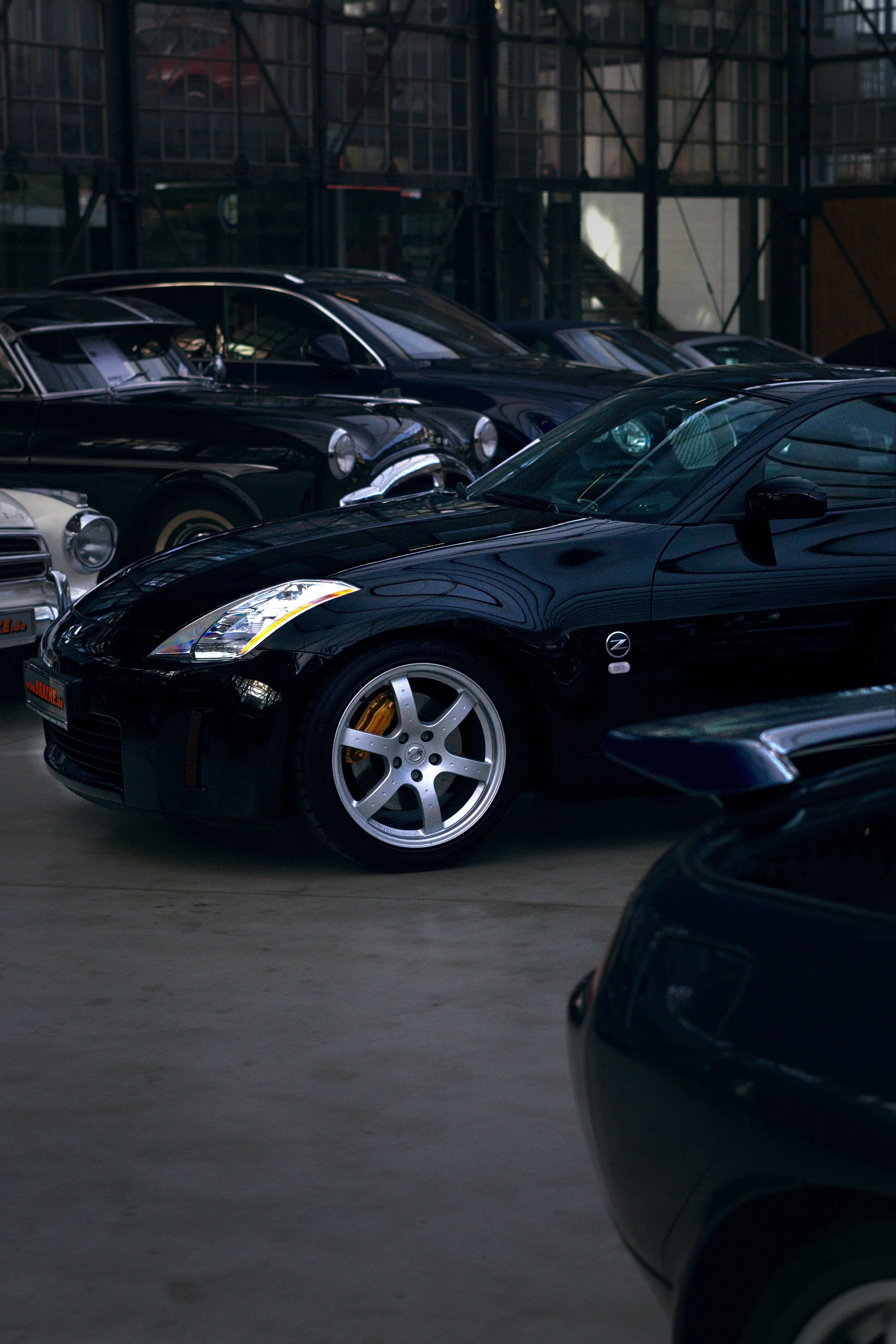 Verschiedene klassische und moderne Autos in einer Garage oder Ausstellungsraum, hauptsächlich schwarze Modelle, mit Blick auf einen schwarzen Nissan 350Z in der Mitte.