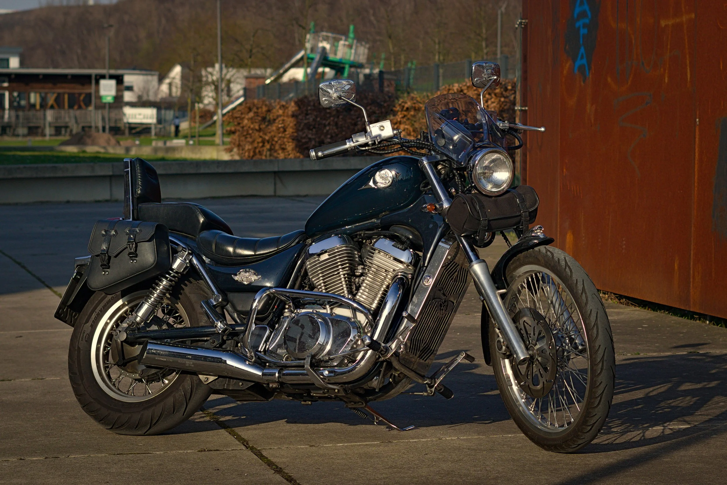 Ein schwarzes Harley-Davidson Motorrad mit Sissy-Bar und Seitentaschen, geparkt auf einer gepflasterten Fläche bei Sonnenuntergang.