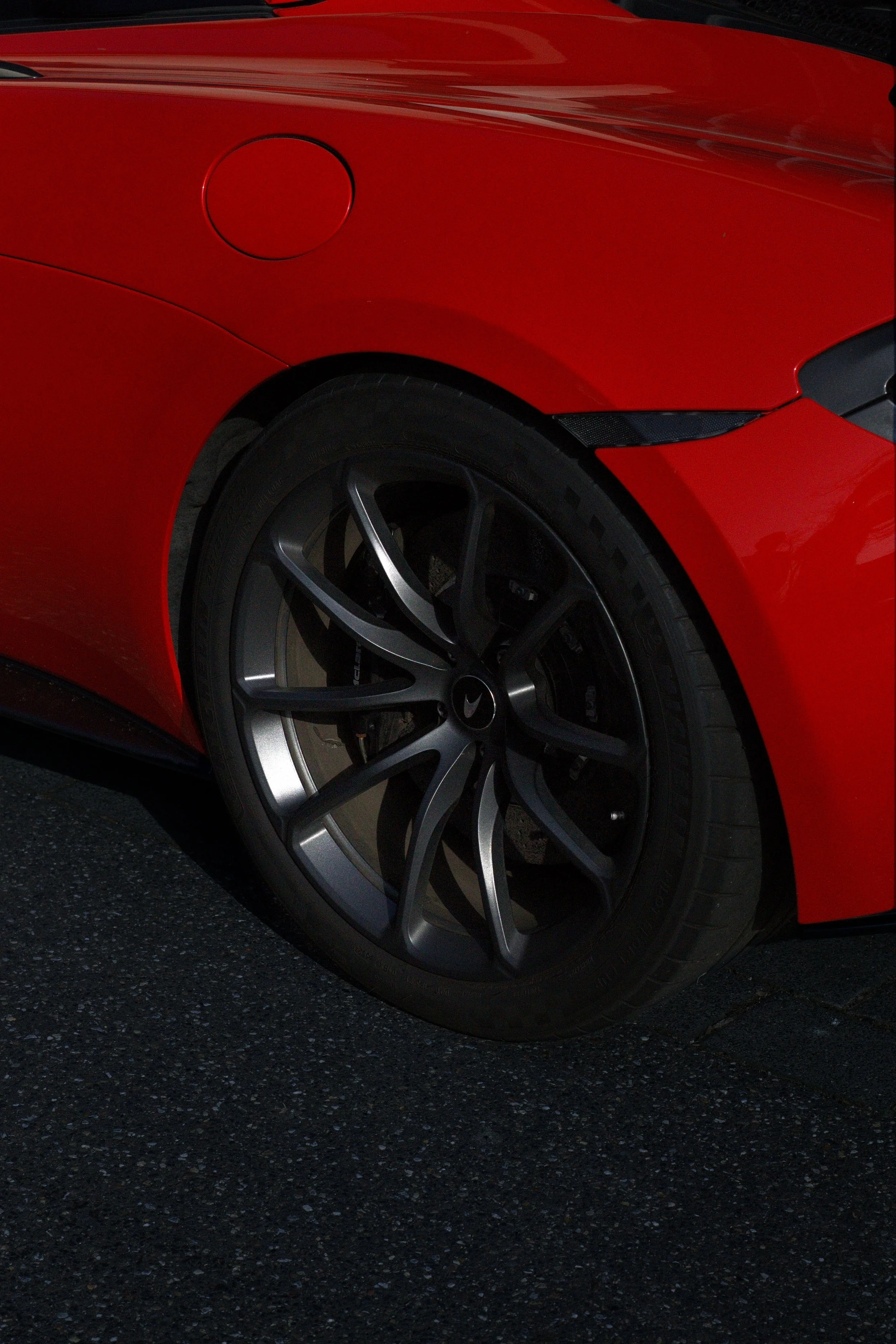Nahaufnahme eines roten Sportwagens mit schwarzen Felgen auf Asphalt.