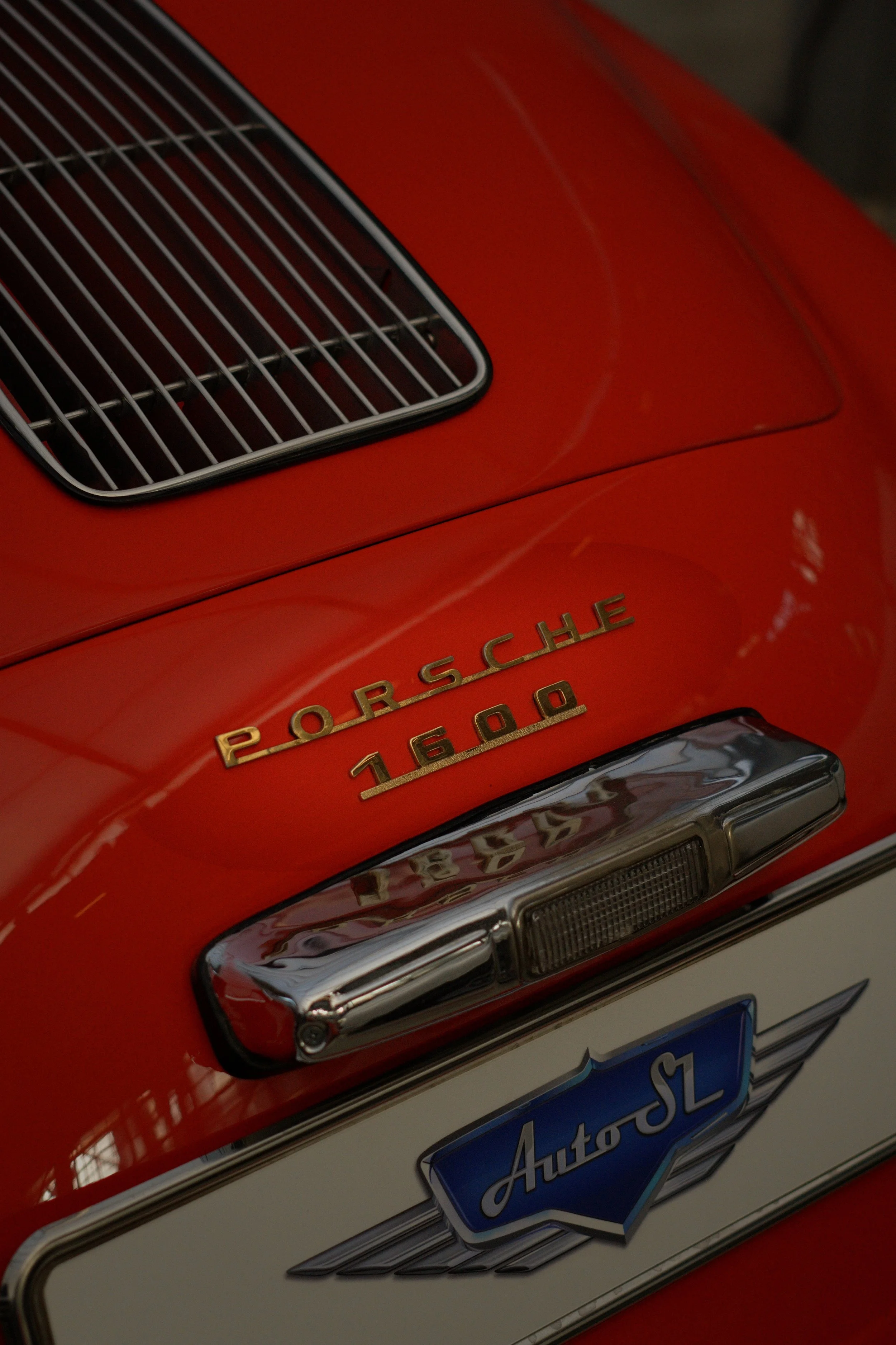 Nahaufnahme eines roten Porsche 1600 Autos mit Chromdetails, Porsche-Emblem und einem AutostL-Plakette.