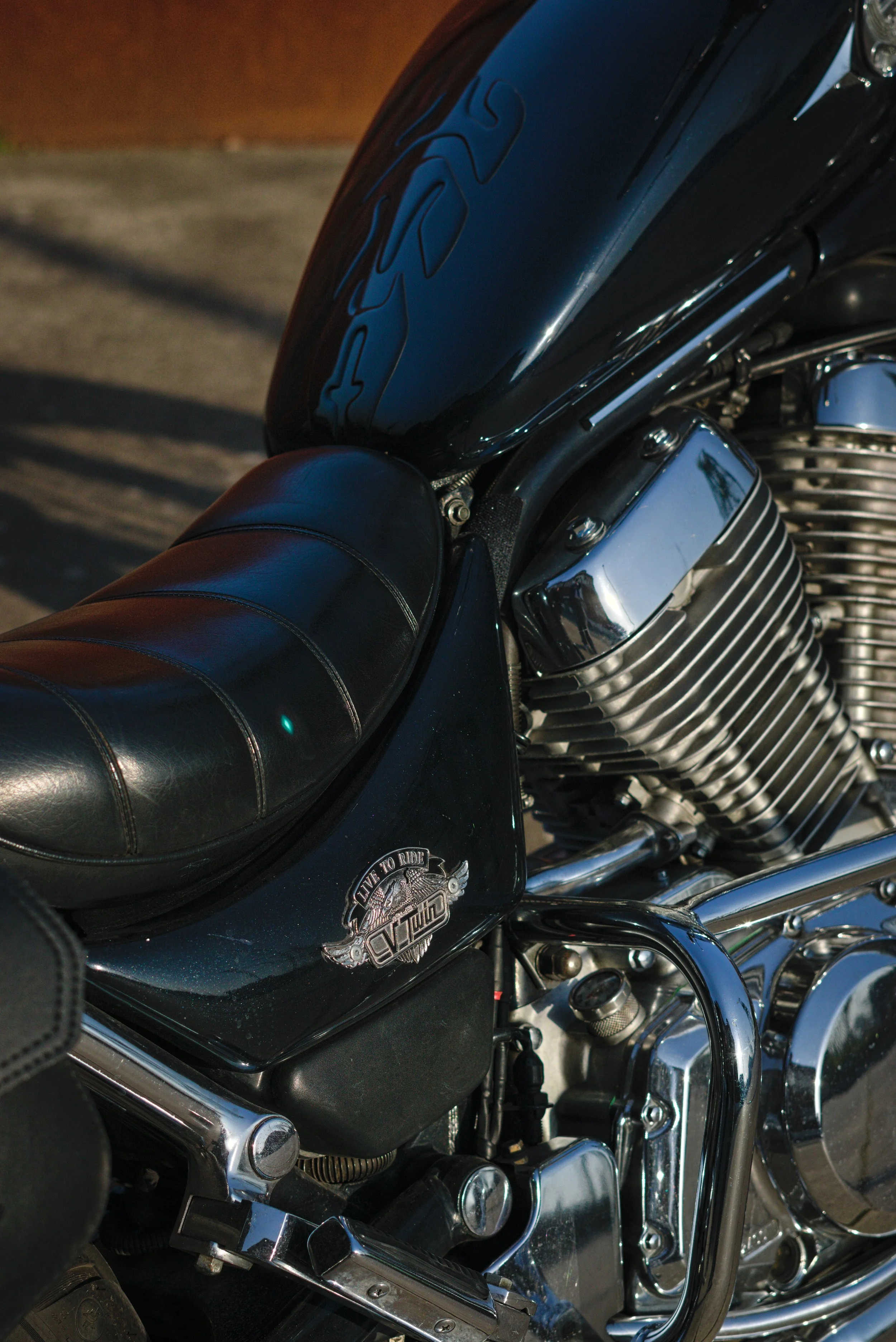 Nahaufnahme eines schwarzen Motorrads mit Chromteilen und Sattel, reflektierender Oberfläche und einem Aufnäher mit dem Schriftzug 'Live to Ride'.