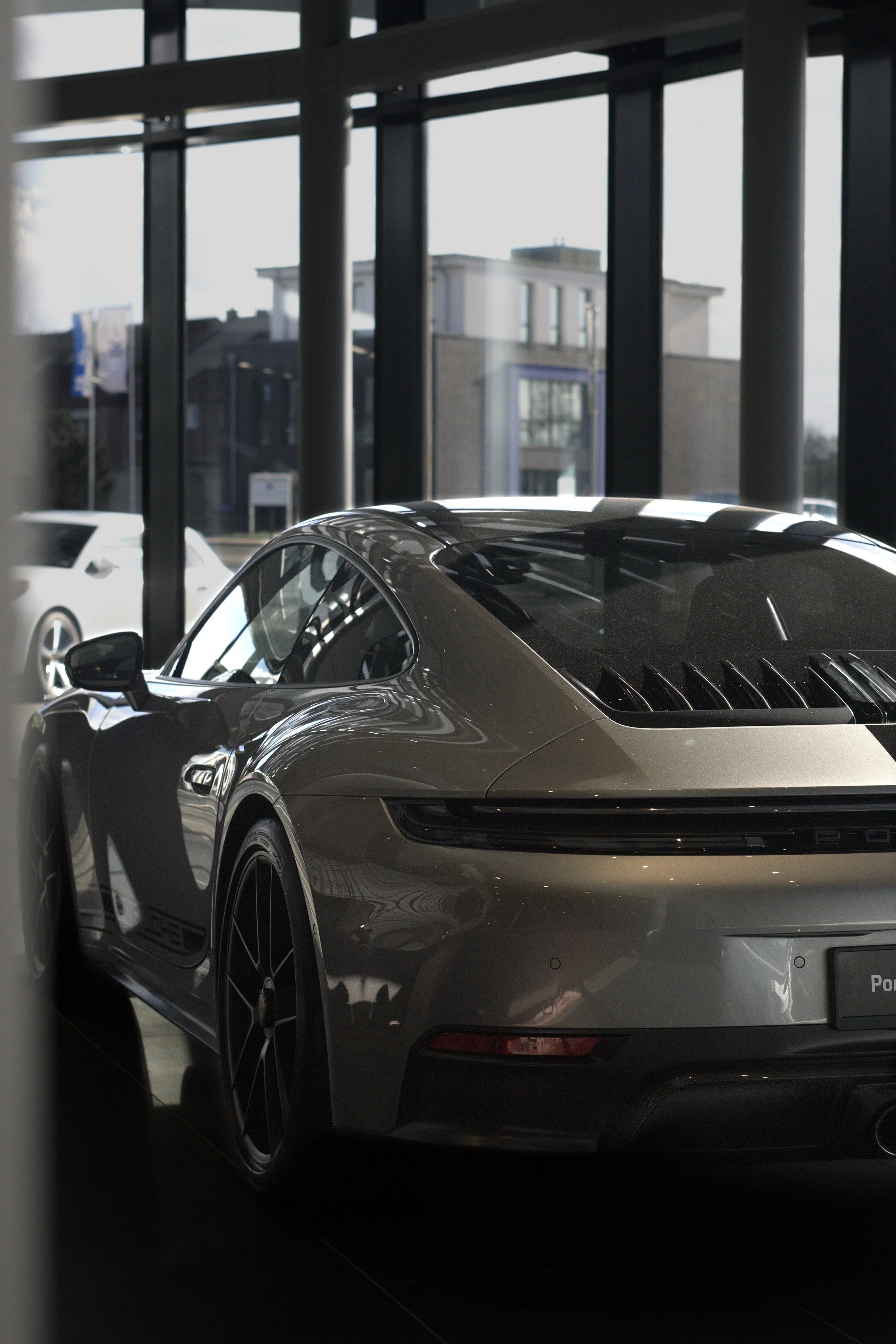 Ein Porsche-Sportwagen steht in einem Autohaus, im Hintergrund sind große Fenster und ein Gebäude außerhalb sichtbar.