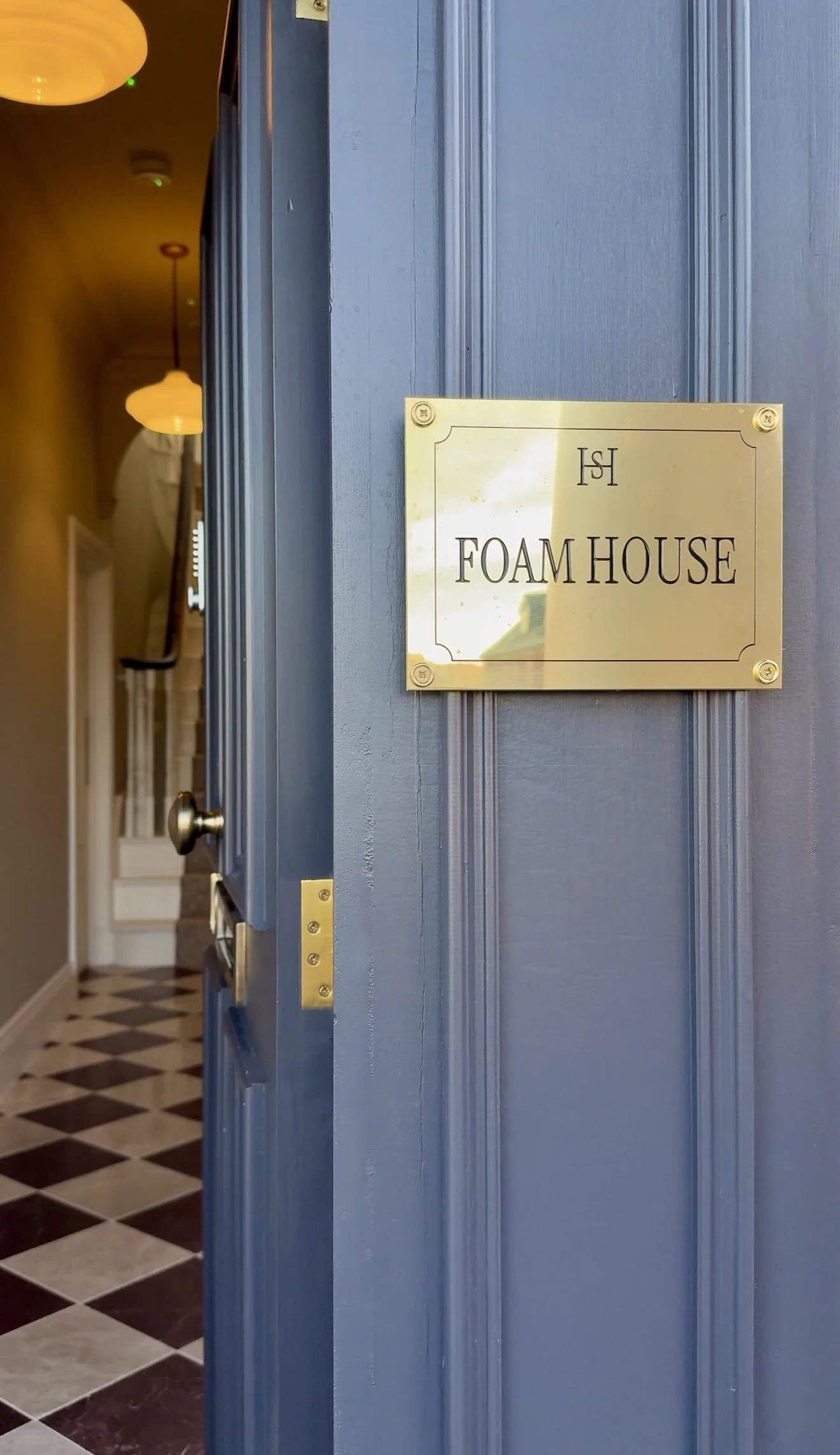 Open blue door with a gold sign that reads "Foam House" inside a building, with hallway and stairs visible in the background.