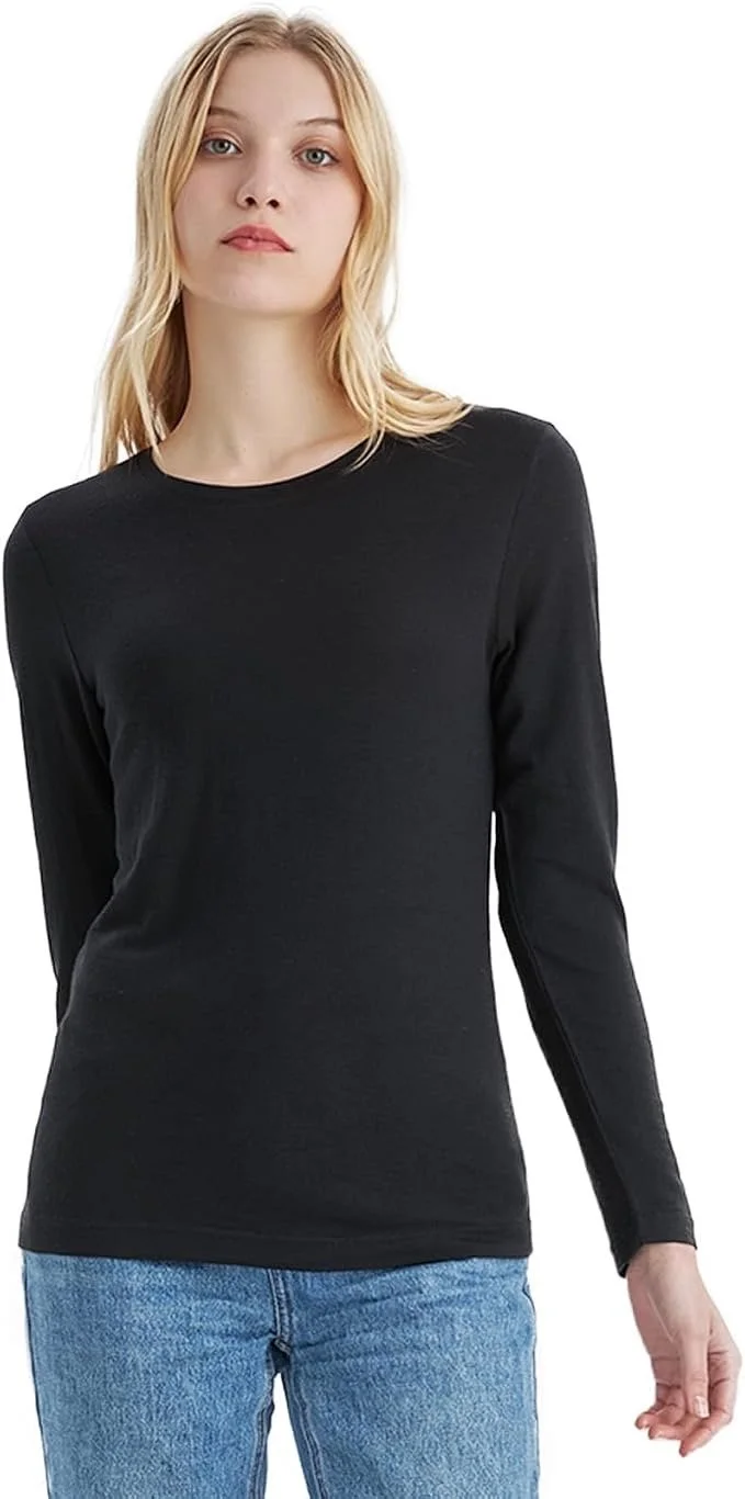 Woman with blonde hair wearing a black long-sleeve shirt and blue jeans, standing against a white background.