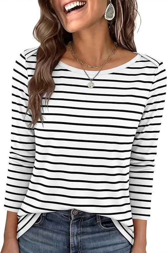A woman wearing a white and black striped long-sleeve shirt, with wavy brown hair, smiling, wearing layered necklaces and a large earring, and blue jeans.