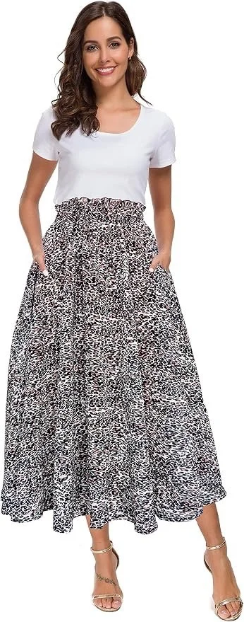 A woman with long wavy brown hair wearing a white t-shirt, a high-waisted black and white animal print maxi skirt, and beige high-heeled sandals. She is smiling and posing with her hands in the pockets of her skirt.