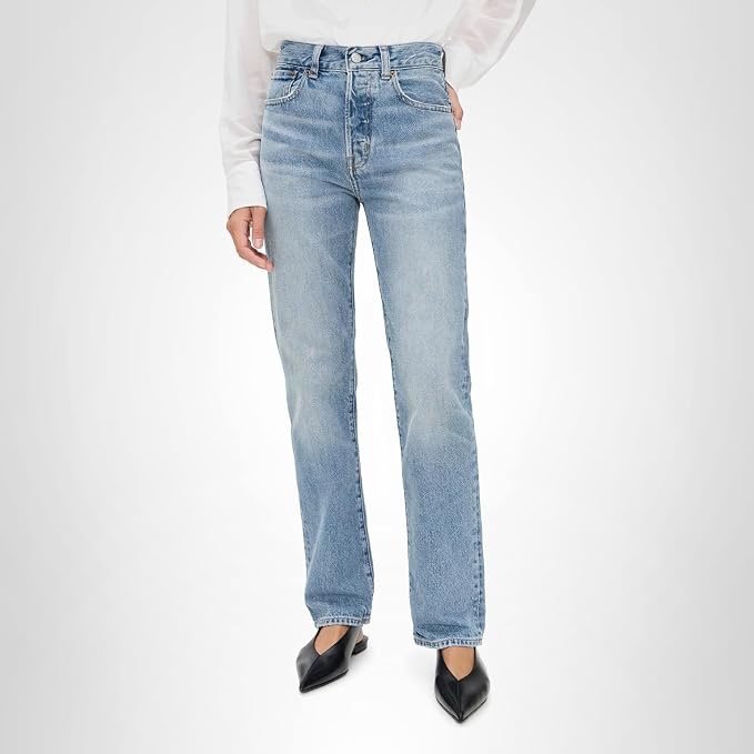 Person wearing light blue high-waisted jeans, black pointed-toe shoes, and a white top. The photo is taken against a plain white background.