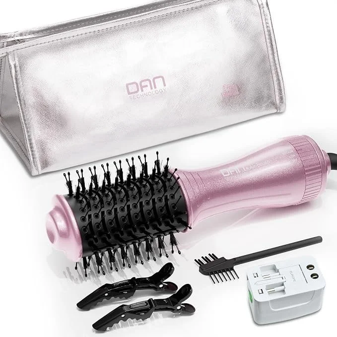 Pink electric hair brush with black vented round brush head, two black clip clasps, a small black cleaning rake, and a white power adapter, all on a white surface with a silver carrying case in the background.