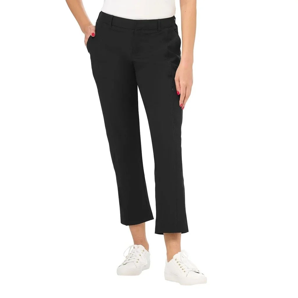 Close-up of a woman wearing black pants, white top, and white sneakers, with one hand in her pocket and the other resting by her side.