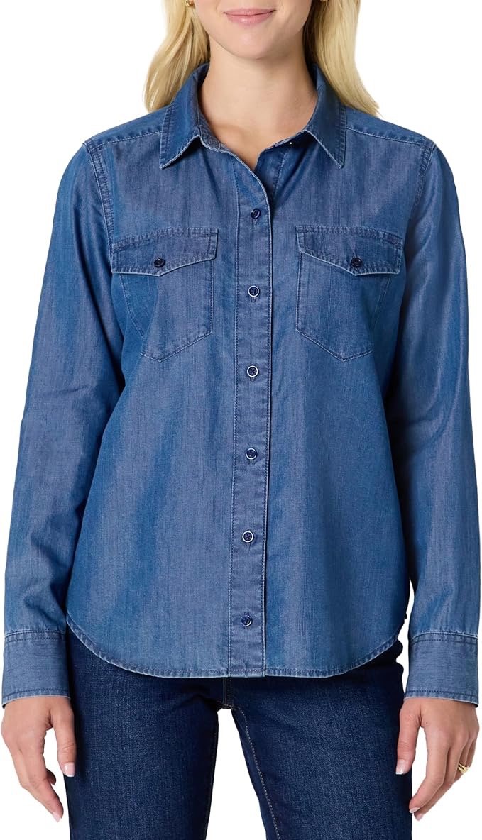 Woman wearing a blue denim button-up shirt with chest pockets, standing against a plain background.