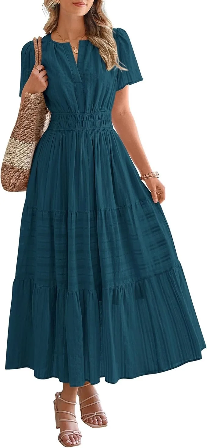 A woman wearing a teal maxi dress with short puffed sleeves and a cinched waist, holding a large woven tote bag and wearing strappy beige high heels.