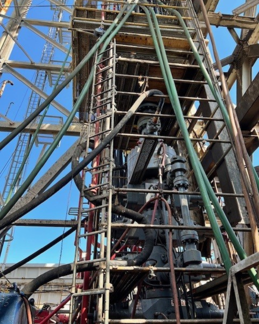 Construction site with scaffolding, pipes, and machinery against a clear blue sky.