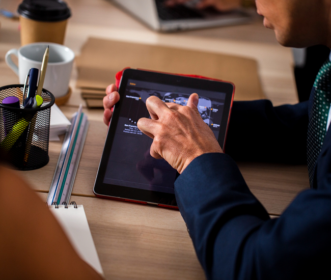 A person in a suit using a tablet to edit a video at a desk with office supplies.