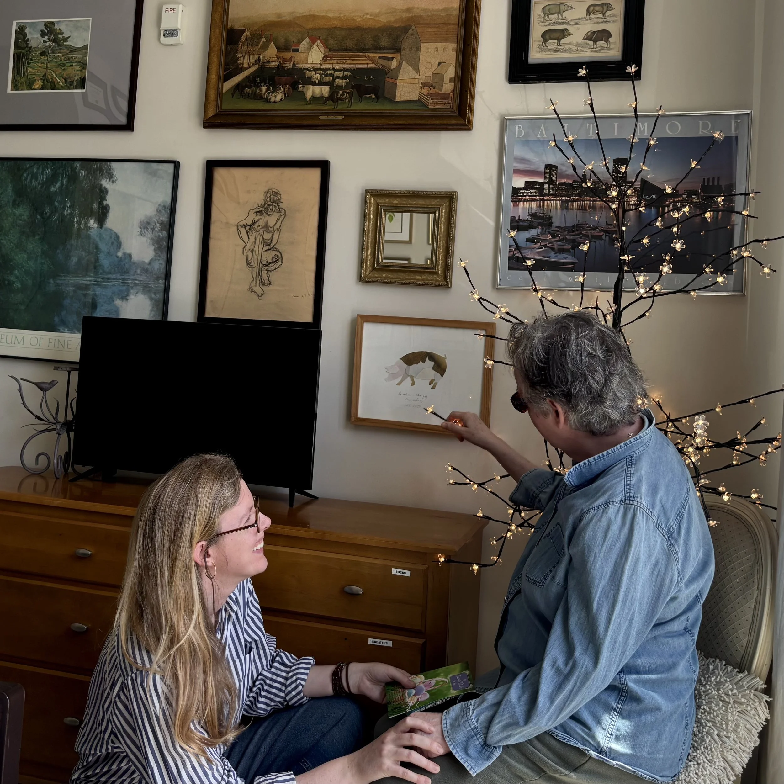 A woman with long blonde hair and glasses hands a card to a woman with gray hair, in an assisted living memory care facility.