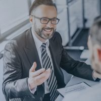 A man in a suit and glasses smiling and talking during a business meeting