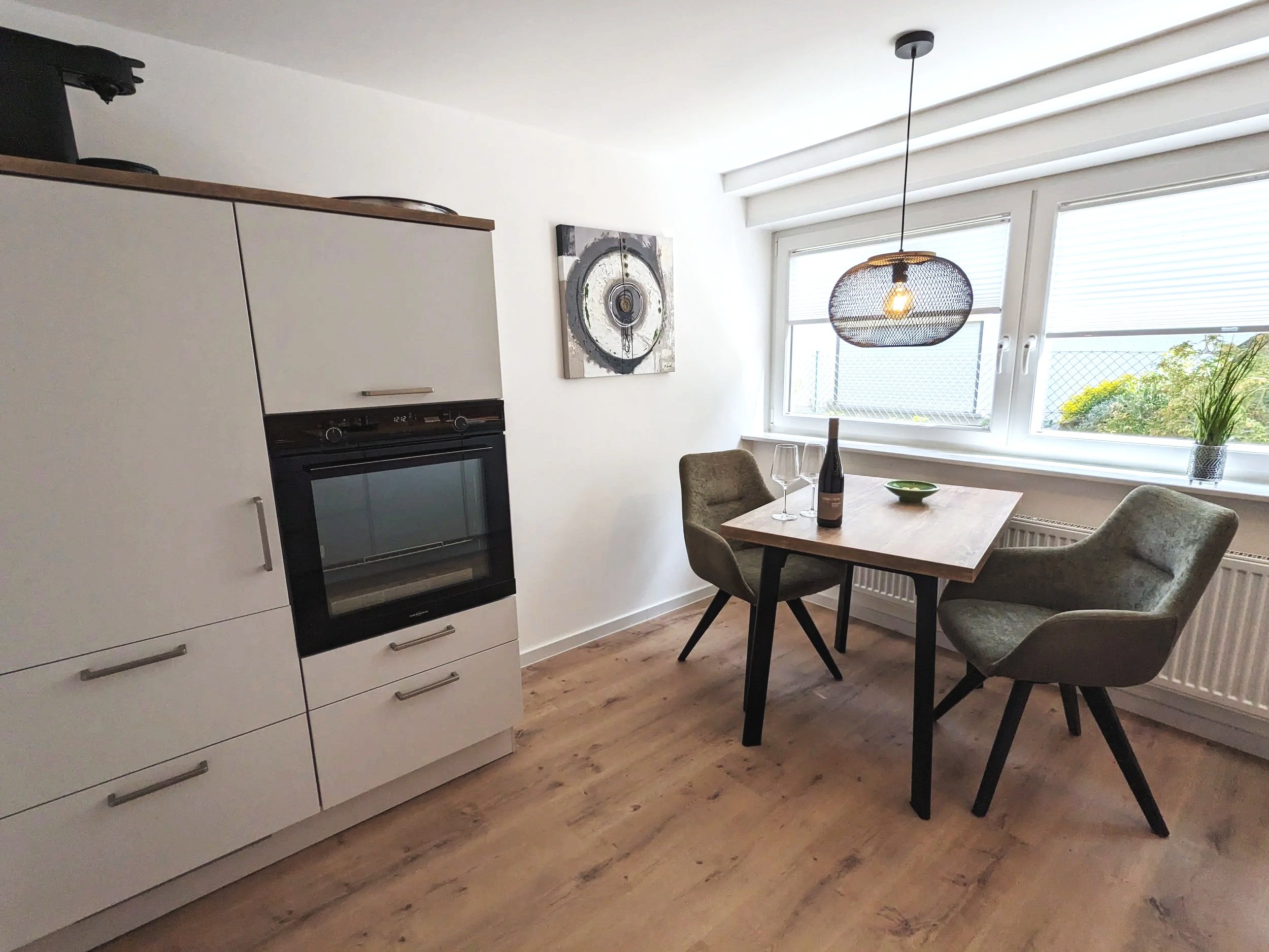 Esszimmer mit großen Fenstern, einem Tisch mit Wein und Gläsern, einem Stuhl, moderner Beleuchtung und einem Gemälde an der Wand.