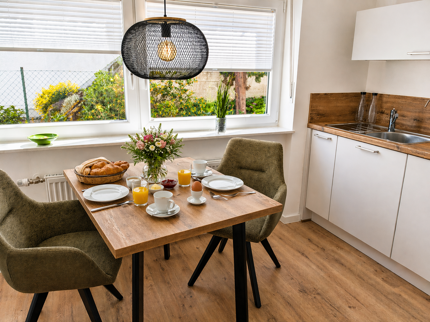 Ein Frühstückstisch mit Zeitung, Eiern, Orangen, Kaffee, Keksen und Blumen, in einer modernen, sonnigen Küche