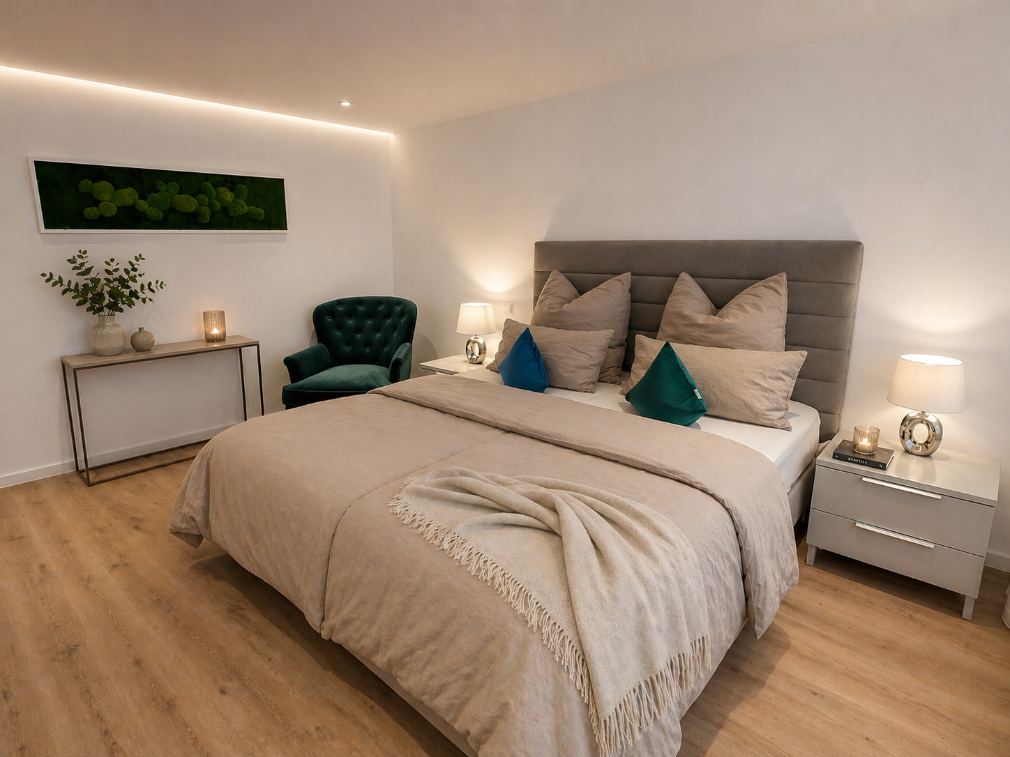 Modernes Schlafzimmer mit Himmelbett, beige Bettwäsche, mehreren Kissen, Nachttischen mit Lampen und Kerzen, grünem Sessel, Wandbild mit Moos und Parkettboden.