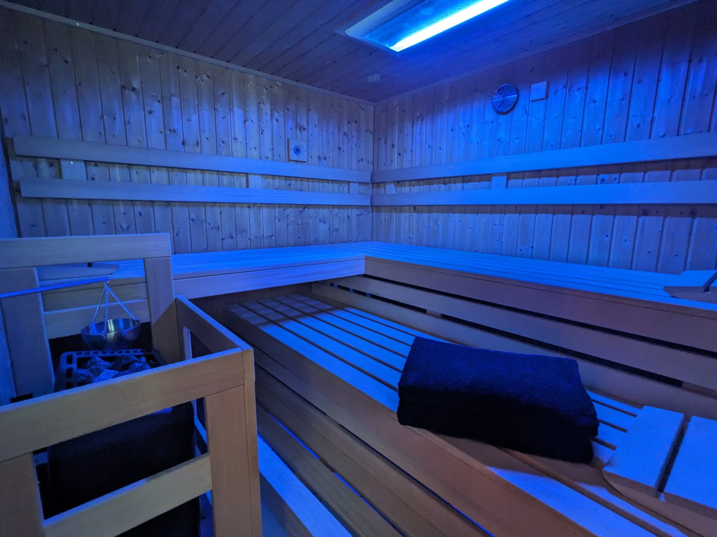 Innenraum einer Sauna aus Holz mit blauer Beleuchtung, Bänken und einem kleinen Tisch