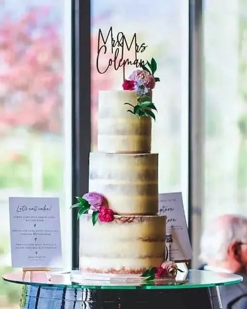 Three-tier semi-naked style buttercream wedding cake with pink and lilac flowers, designed by Bloon & Co. Venue: Primrose Hill Farm, Warwickshire.  Image by @libbyclarkphotography.