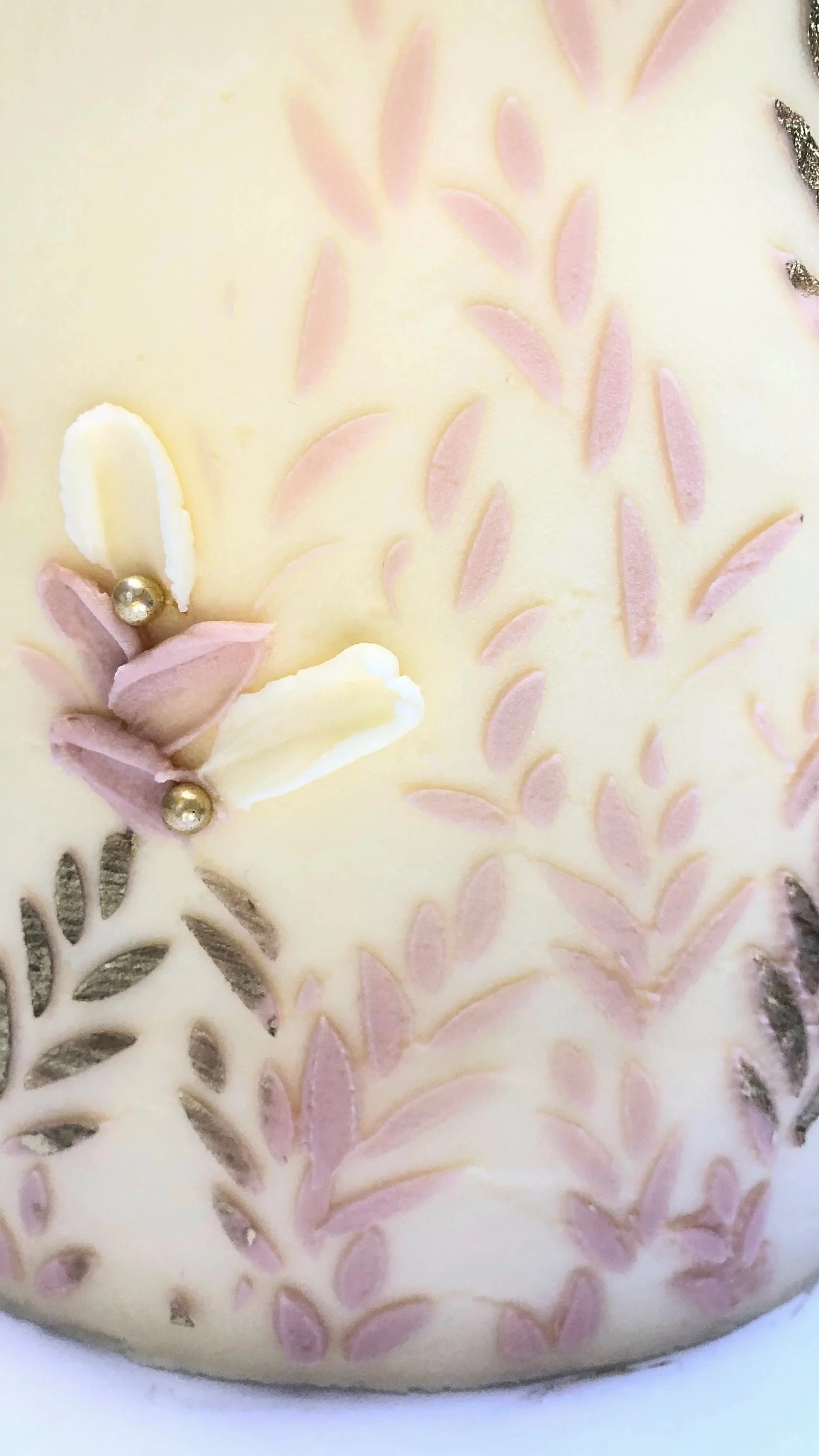 Close-up of an elegant buttercream decorated cake with pink and gold stencilled leaf patterns and small edible pearls. 